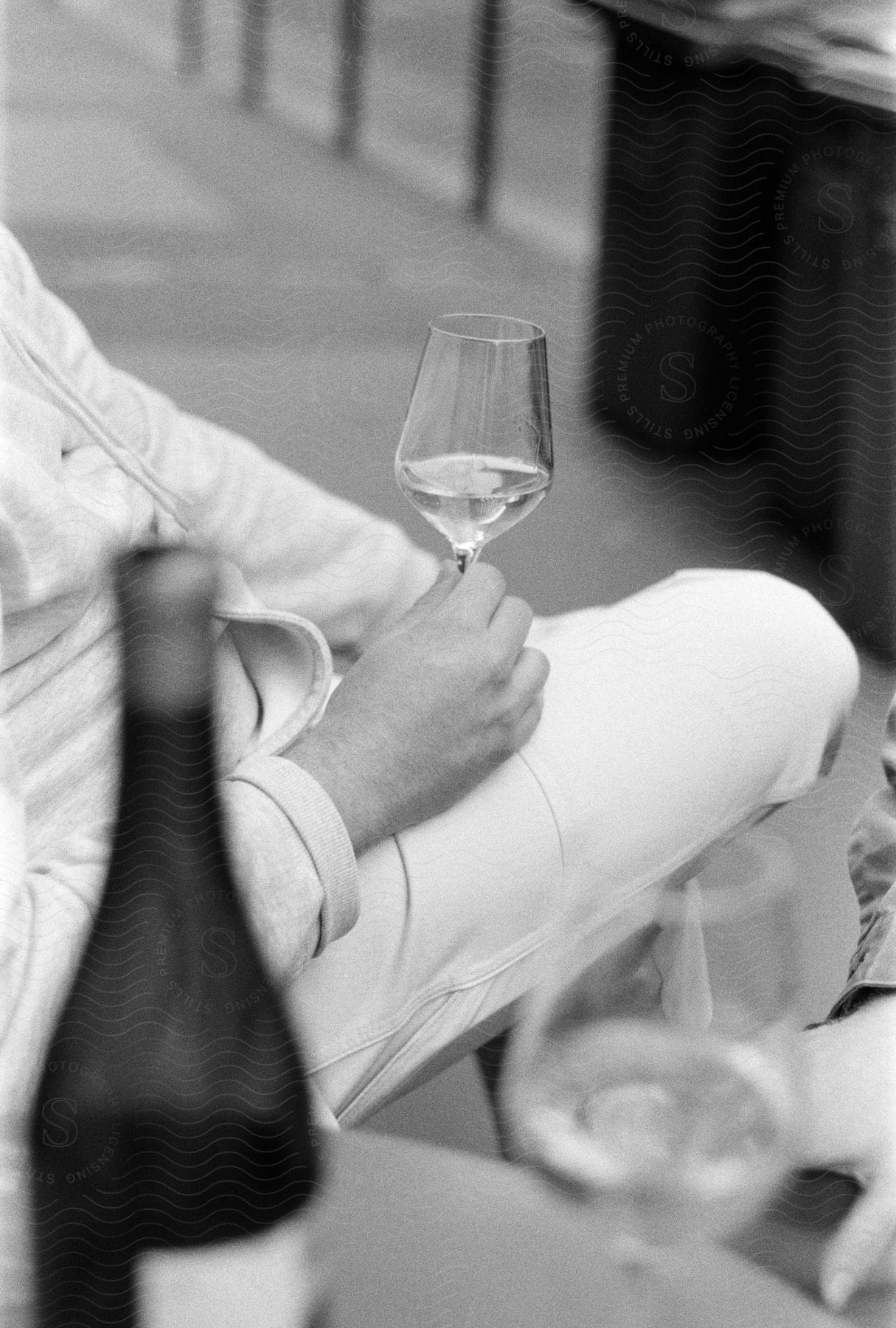 A person is sitting holding a glass of wine in a classic, timeless scene. The setting appears to be outdoors, and the image is in black and white, adding a touch of elegance.