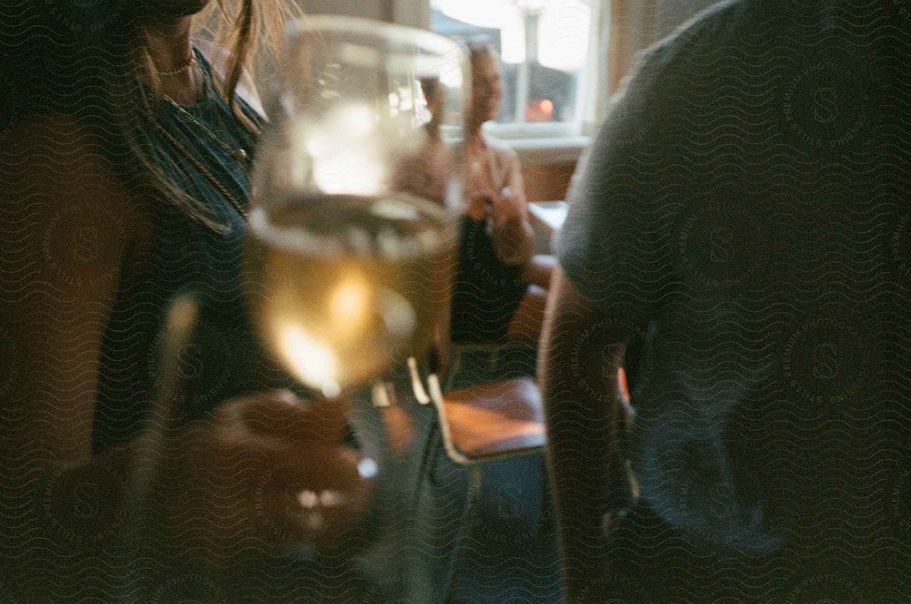 A woman wearing necklaces and a blue shirt holds a glass of wine next to a man wearing a blue shirt in a cafe.