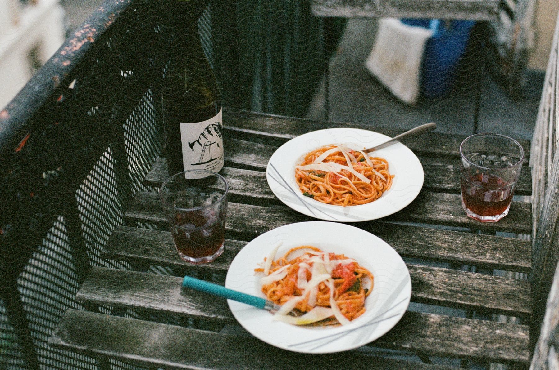 An al fresco meal with two portions of spaghetti, a bottle of wine and two glasses on a rustic wooden table.