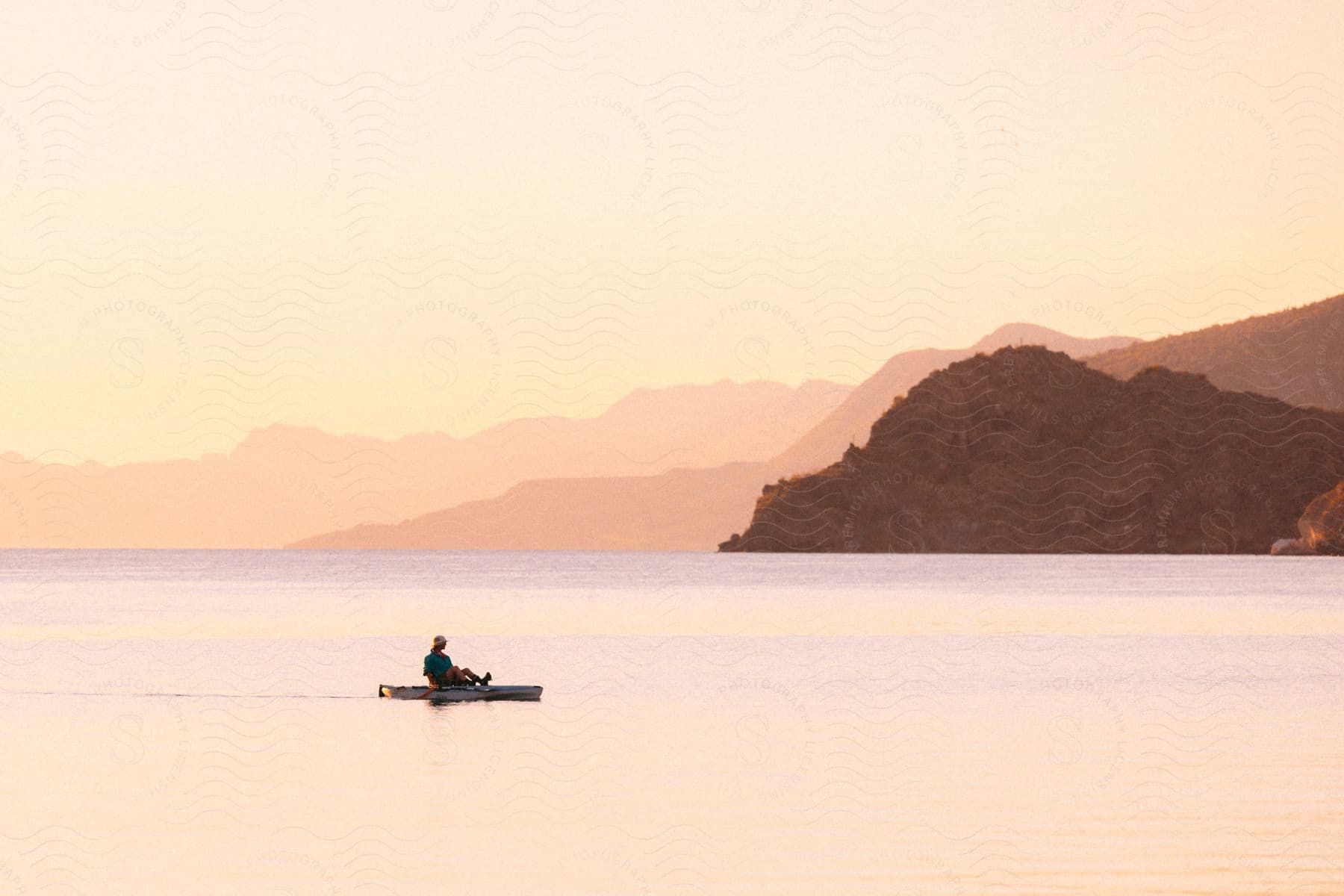A man in a paddleboat before a mountainous coast.