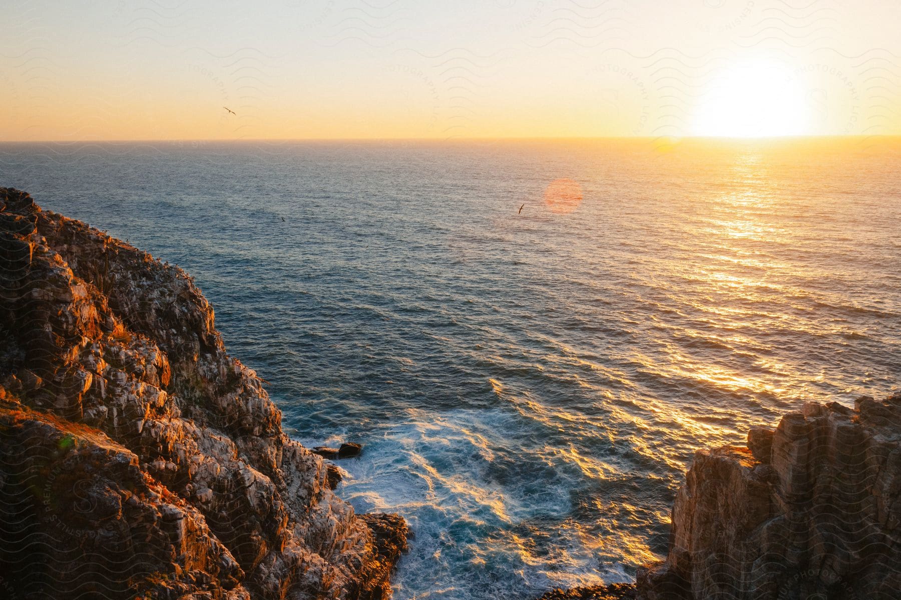 Landscape of an ocean on the edge of a rocky coast with the orange sunrise on the horizon