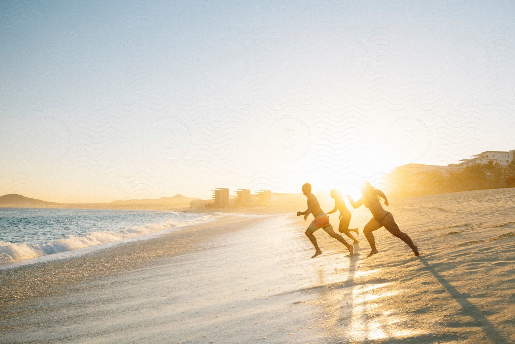 Three people in swimsuits running on a beach towards the ocean on a sunny day.