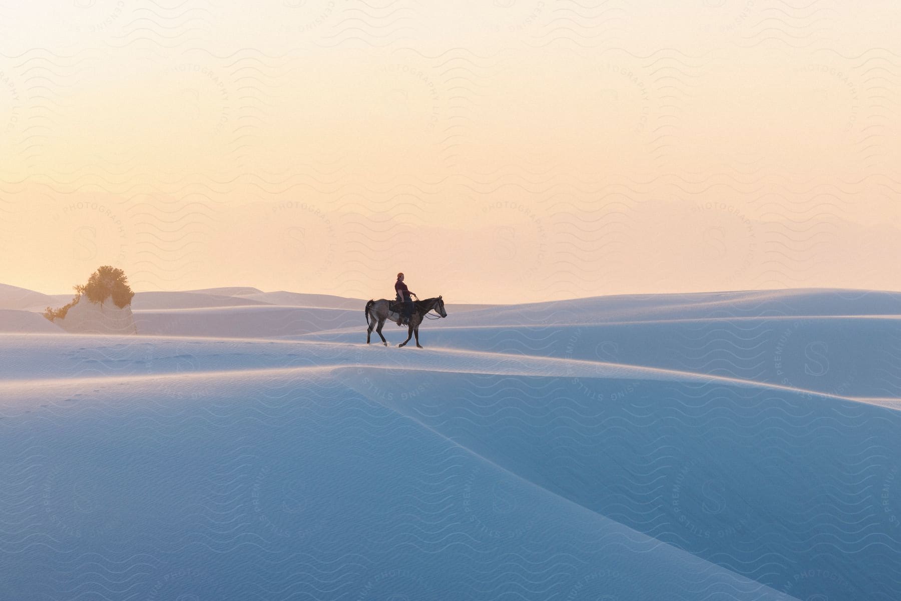 A woman rides a horse on white sand desert at sunset.