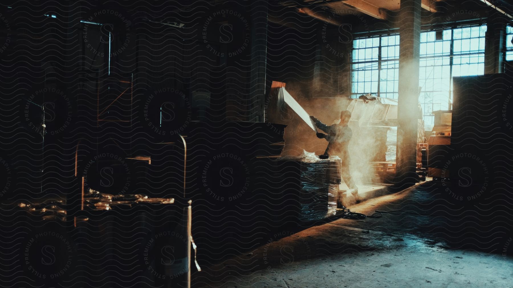 Worker holds sheet while standing in a dimly lit factory on a sunny day.