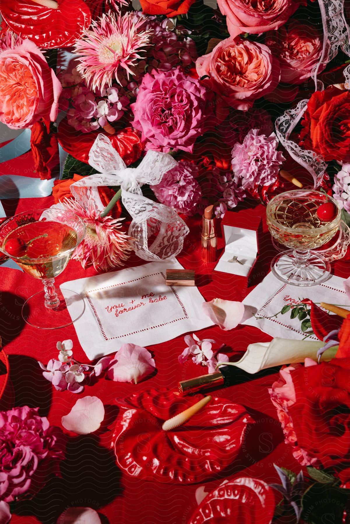 A white cloth on a table with a red cloth and two glasses with drinks and there are many red flowers