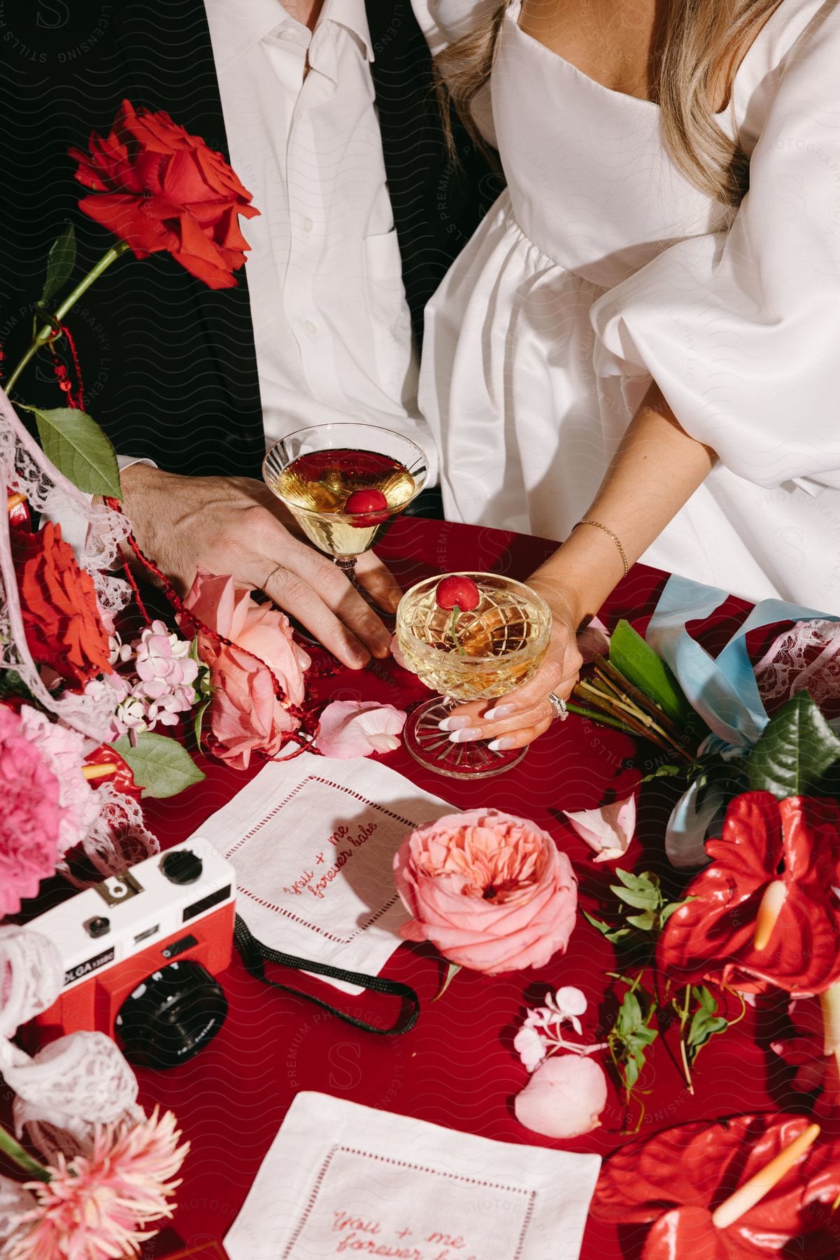 A couple in formal wear toasts with wine glasses surrounded by a variety of flowers