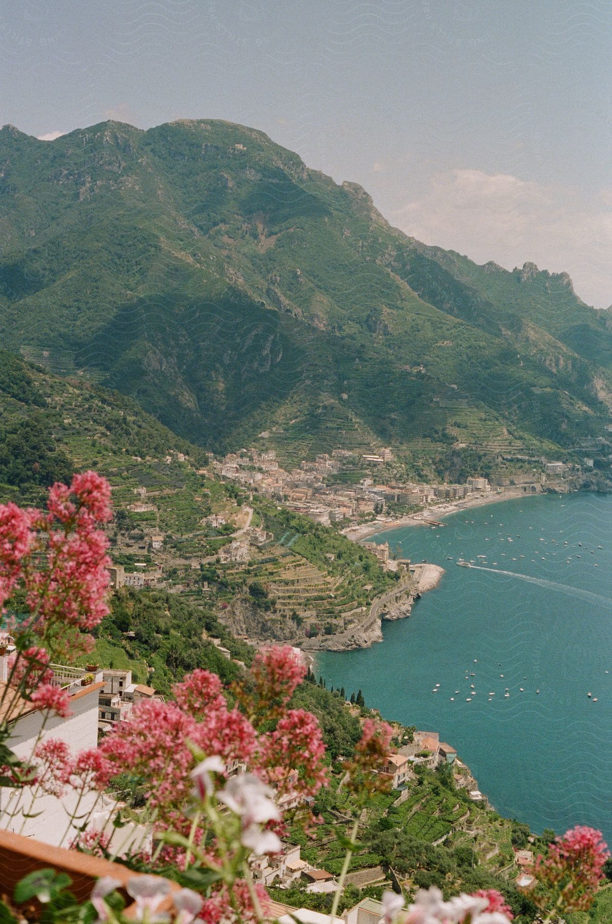 Panoramic view of a coastal city with buildings along mountains and a blue sea in the background.