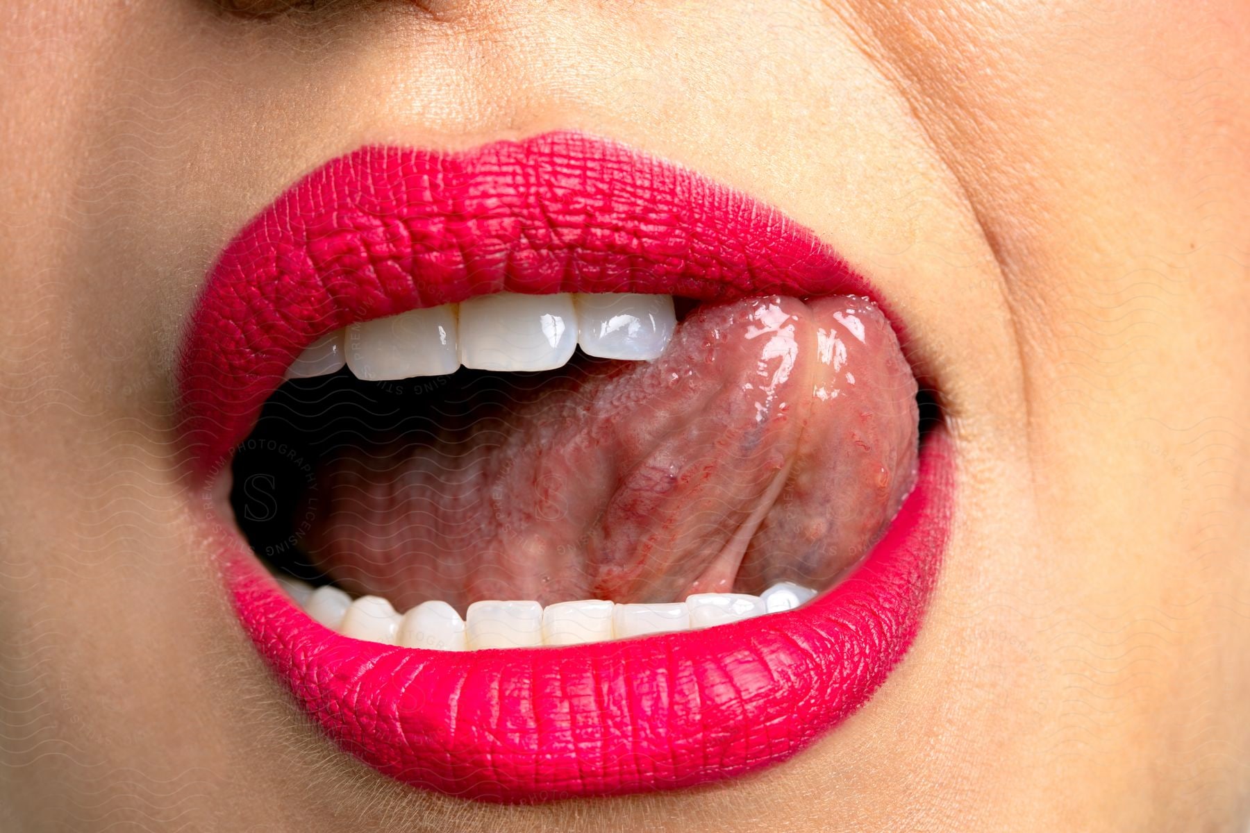 Close-up of a person wearing red lipstick, with their tongue sticking out. The lips are painted with a bright red lipstick, and the teeth are visible.