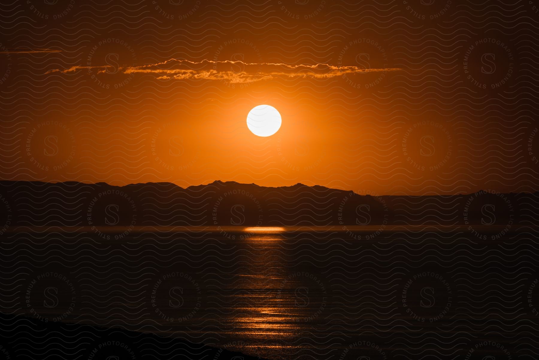 Sunset over the sea with the sun casting a golden glow across the sky and water, silhouetting the distant mountains.