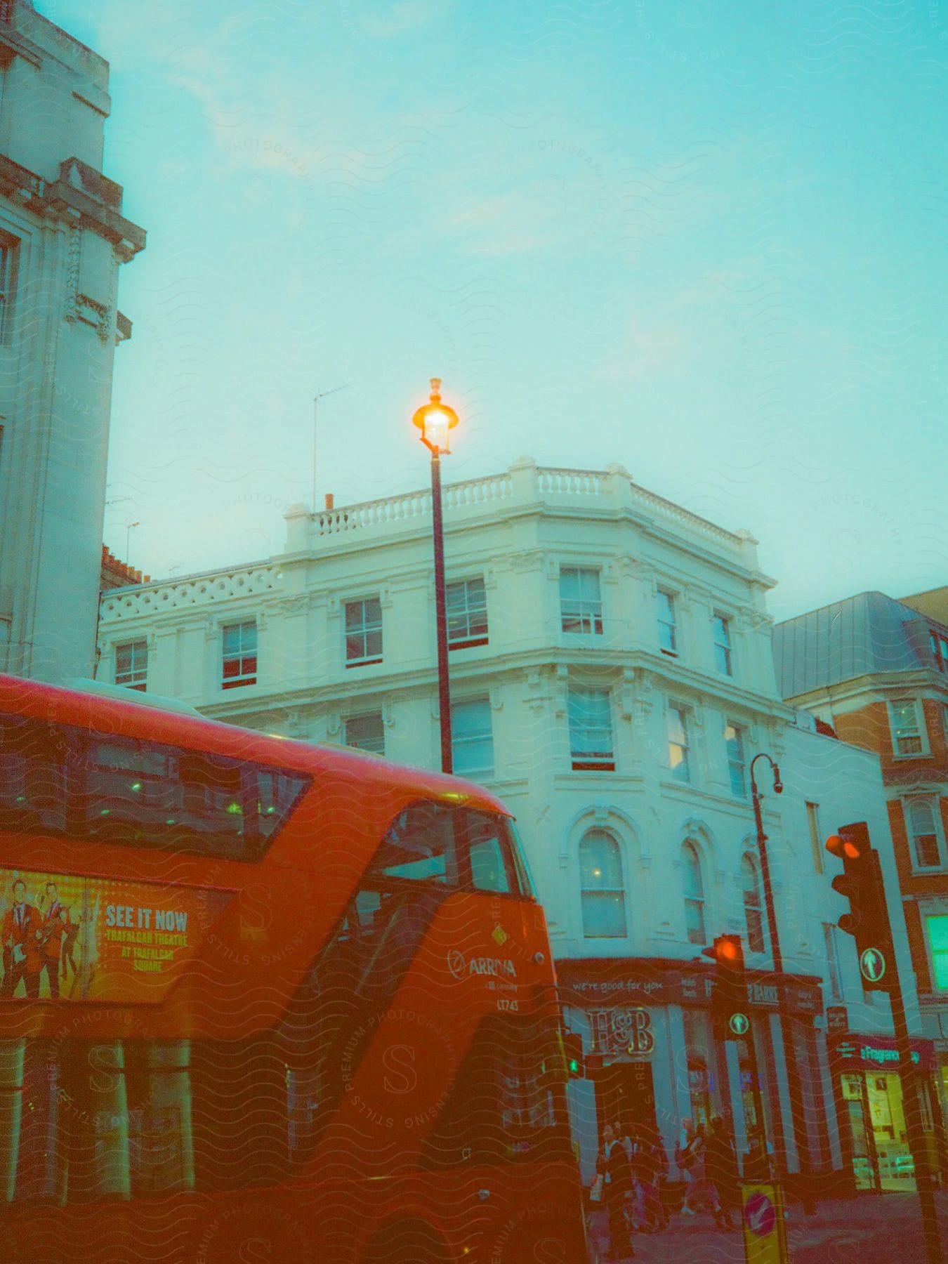 A double-decker bus stopped on a street lined with shops and apartments.