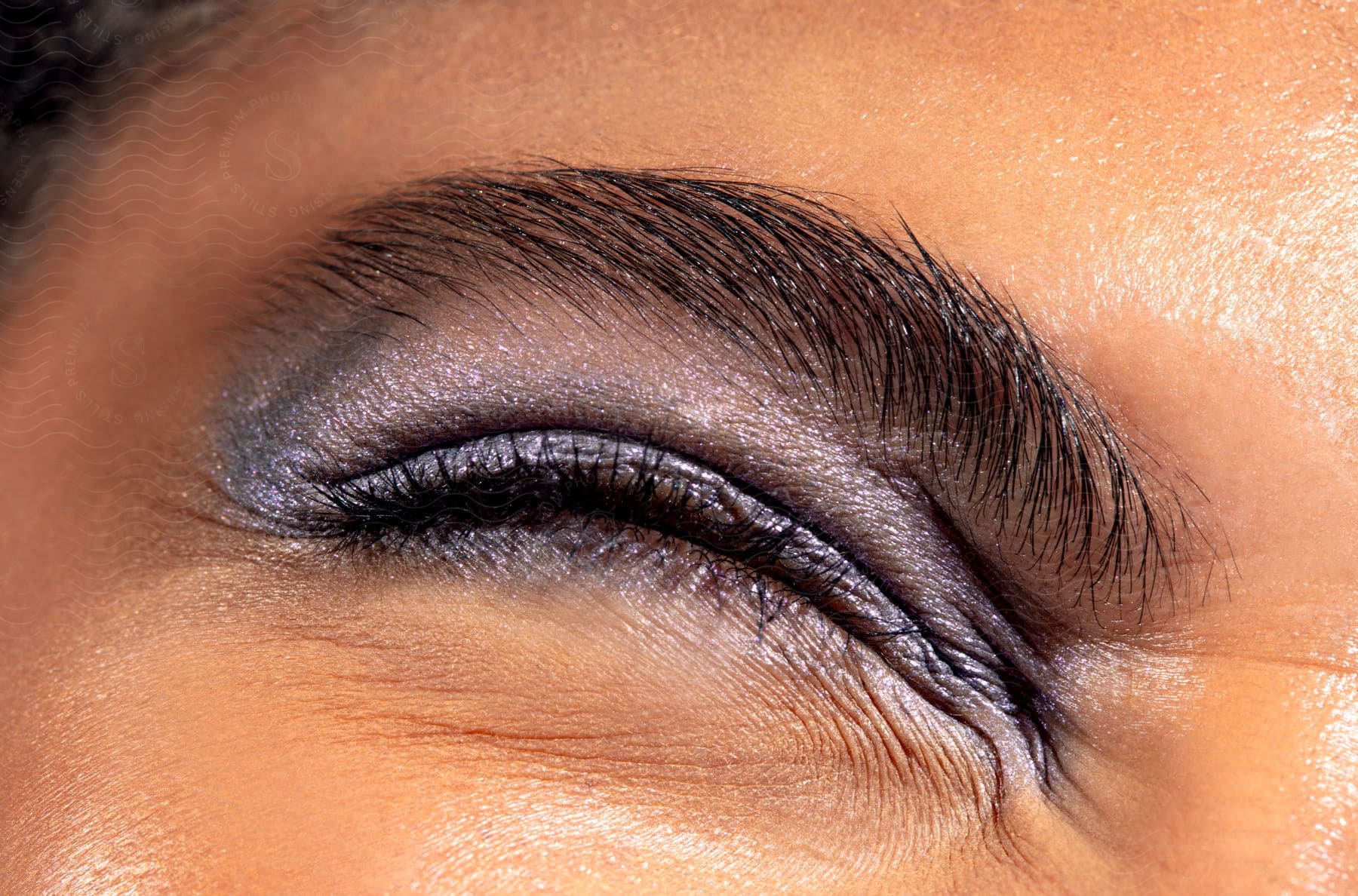 Close-up of a person's eye, beautifully highlighted with metallic eyeshadow and neatly styled eyebrows. The makeup emphasizes the natural colors and textures of the skin.