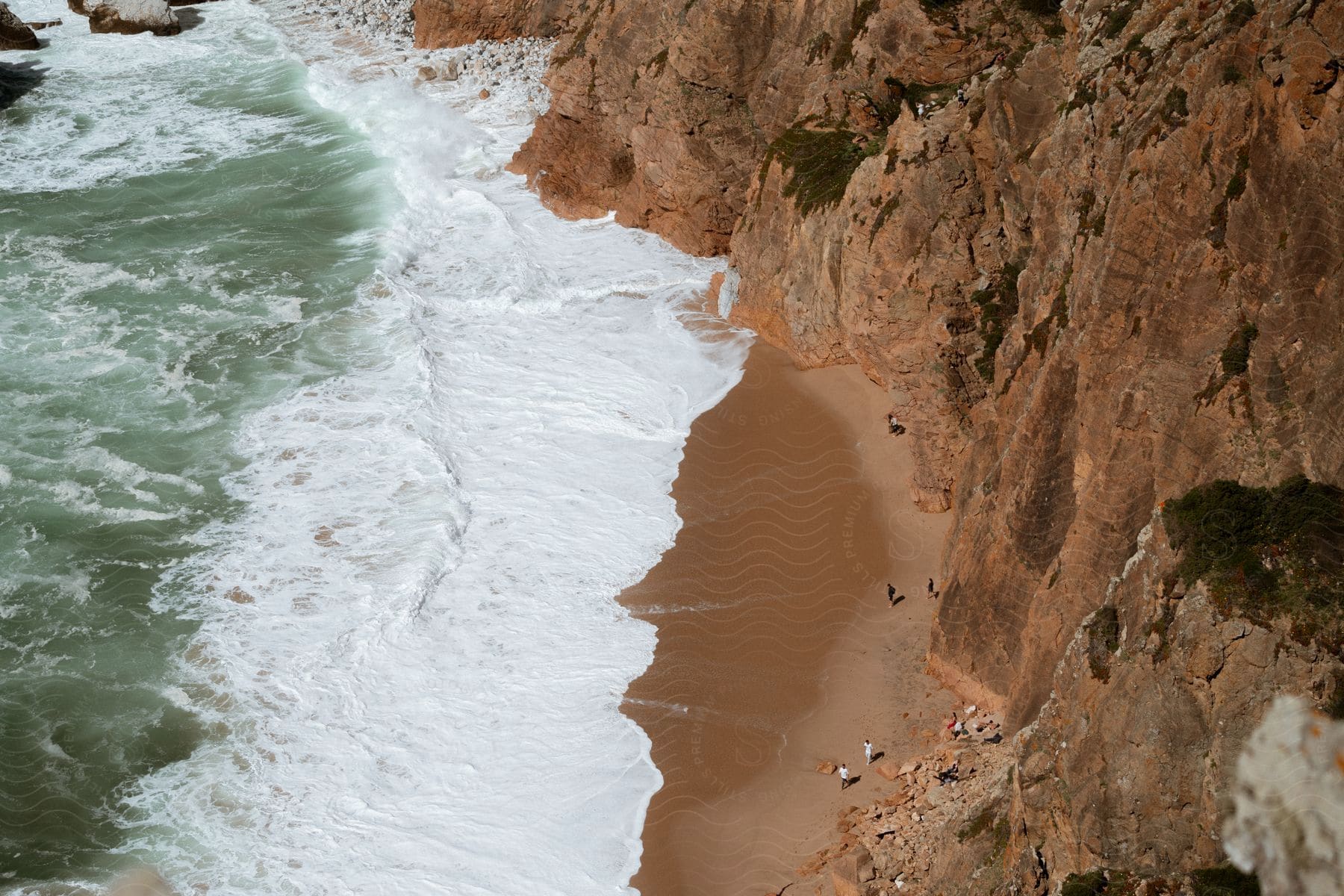 large and foamy ocean waves crashing on a sandy beach next to a cliff.