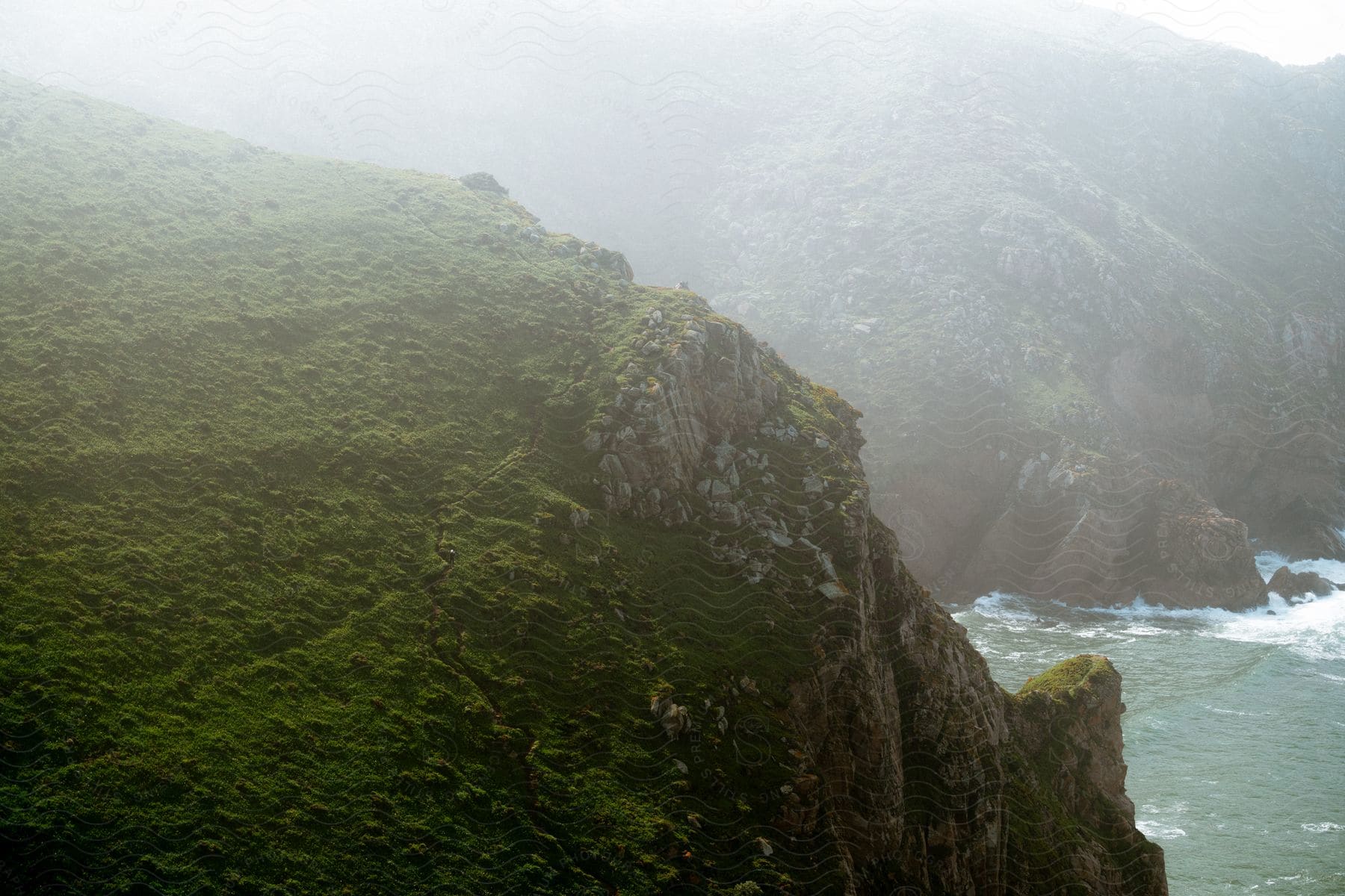 An ocean sits next to a green mountain range on a sunny day.