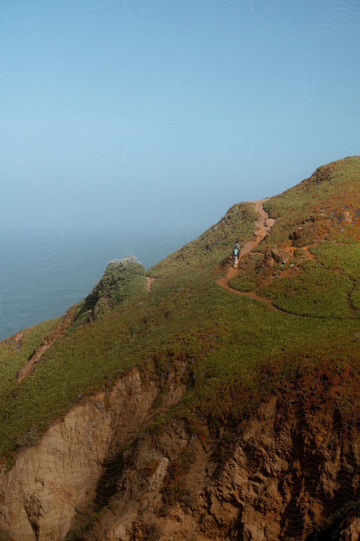 Two people walk on a mountain path overlooking the coast