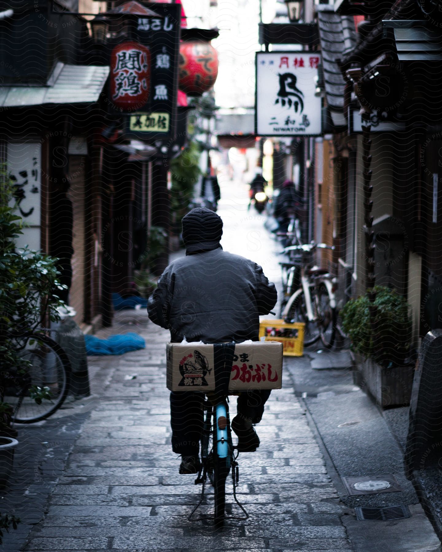 Man riding a bicycle in a paved alley with Asian businesses around