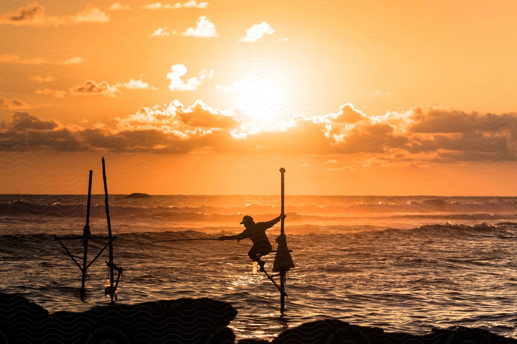 An adult hangs on to a pole with one arm while fishing with the other arm in the ocean at dusk.