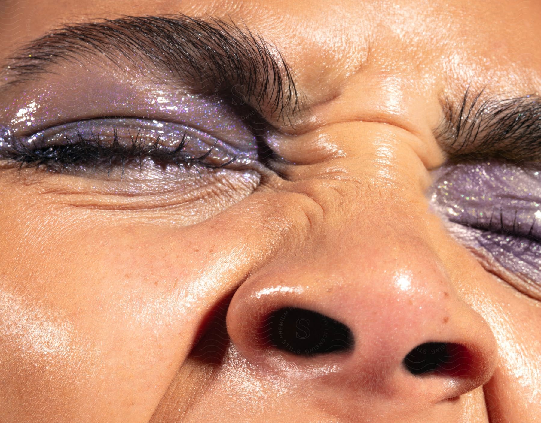 Close-up of a person's closed eyes, with purple eyeshadow applied. The eyebrows are well-defined and the skin looks smooth with a natural glow.