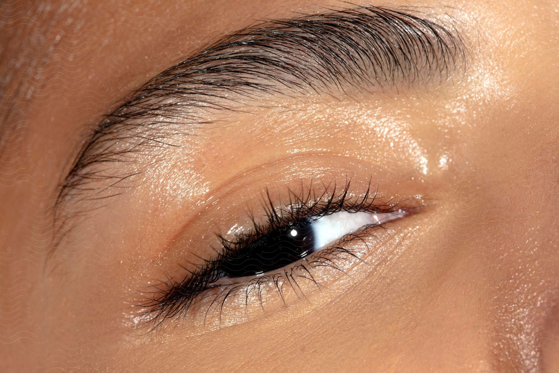 A person's eye with black iris and his skin is reflecting natural light