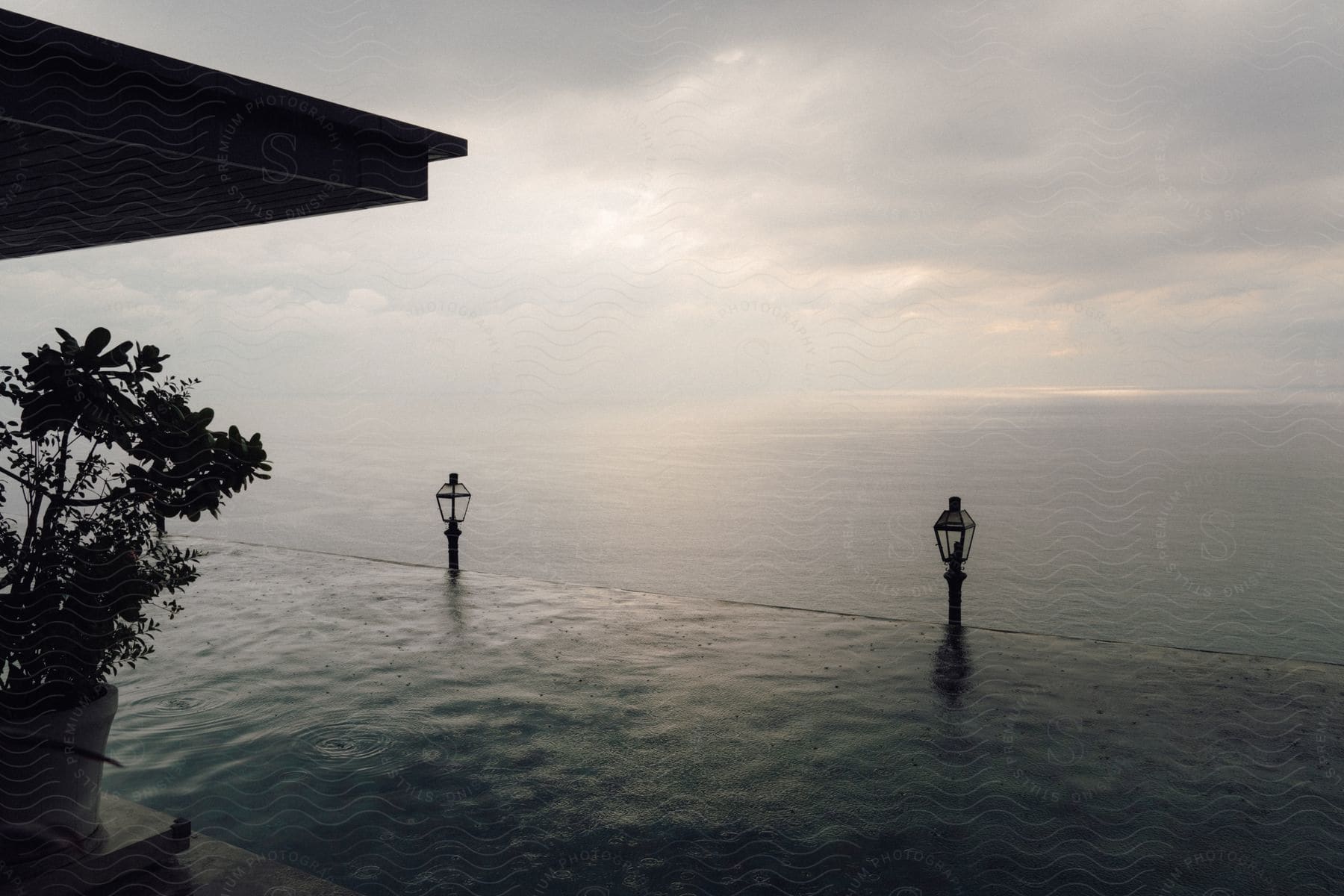 A serene view of an infinity pool overlooking a calm sea under a cloudy sky.