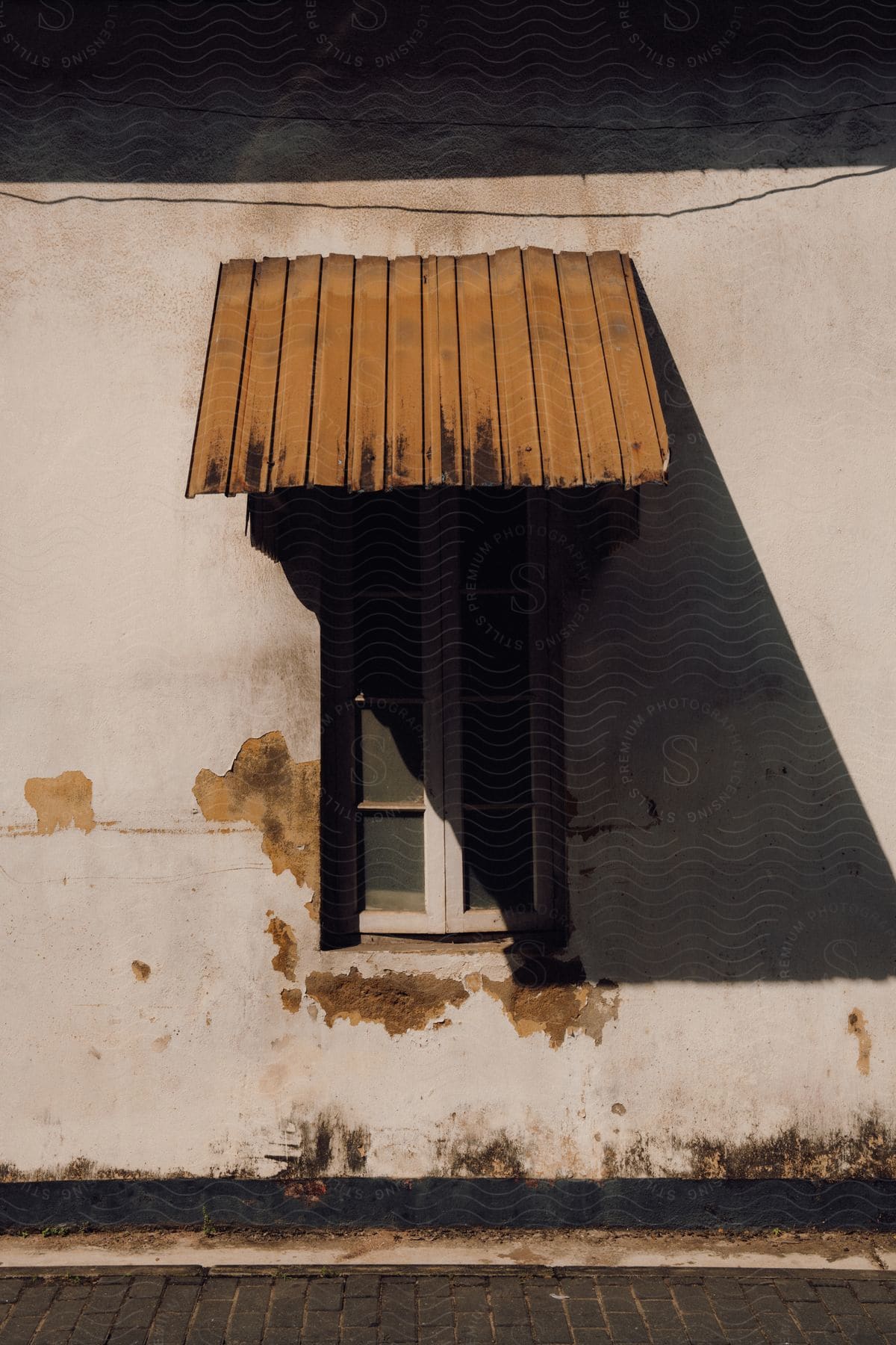 An old and worn window, with a wooden cover above, on an old decaying house.