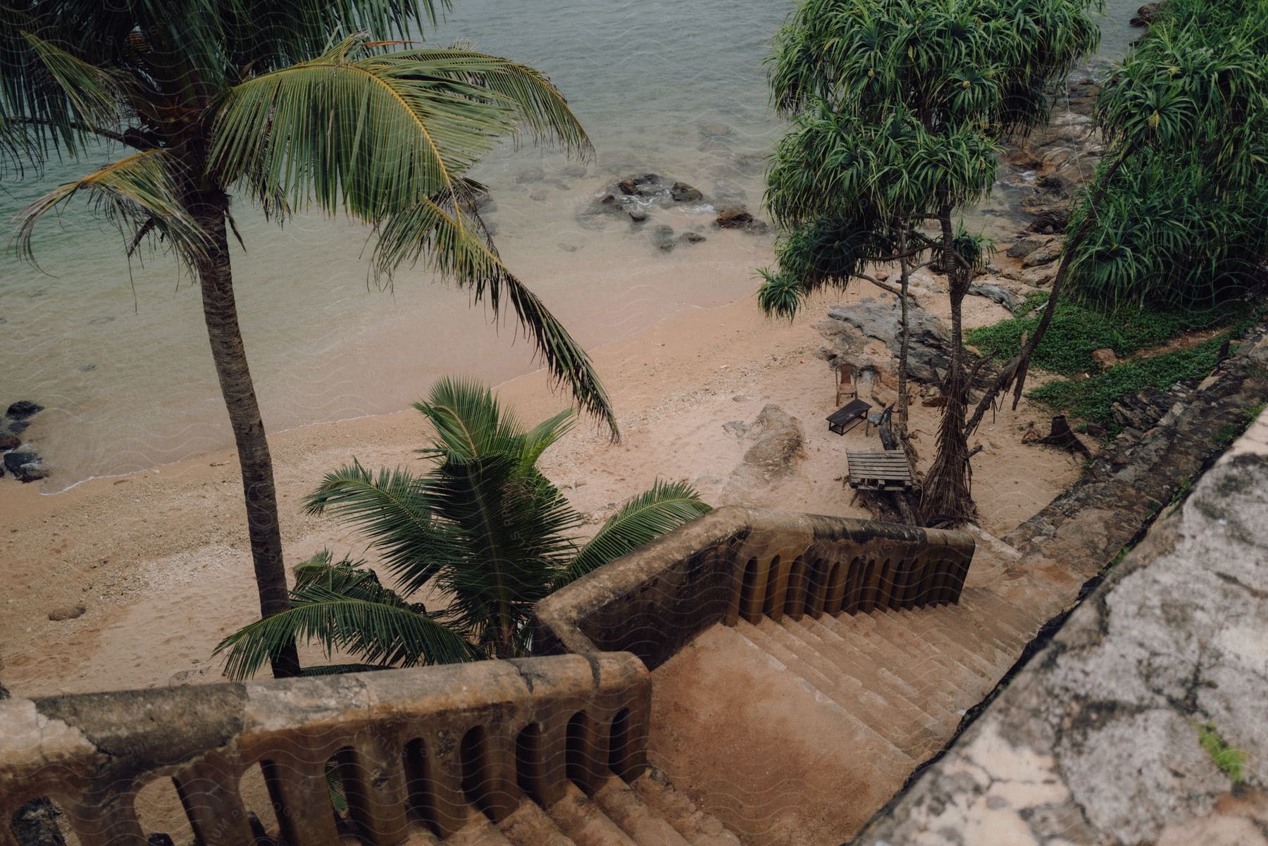 Stock photo of a set of weathered wooden stairs leads down a grassy bluff to a sandy beach. the ocean is a calm blue in the distance.