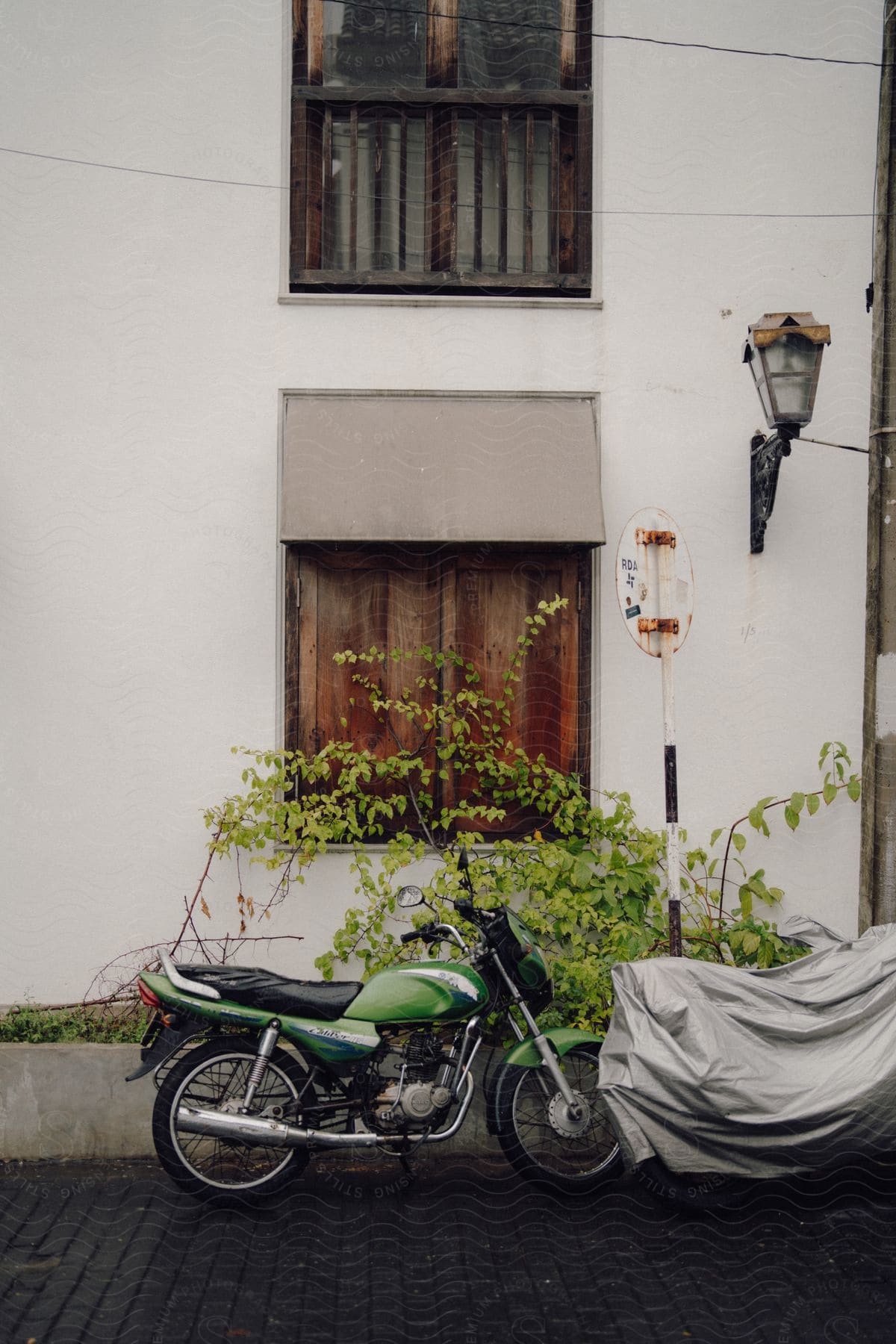 A green motorcycle is parked diagonally in front of a white building with a gray awning.