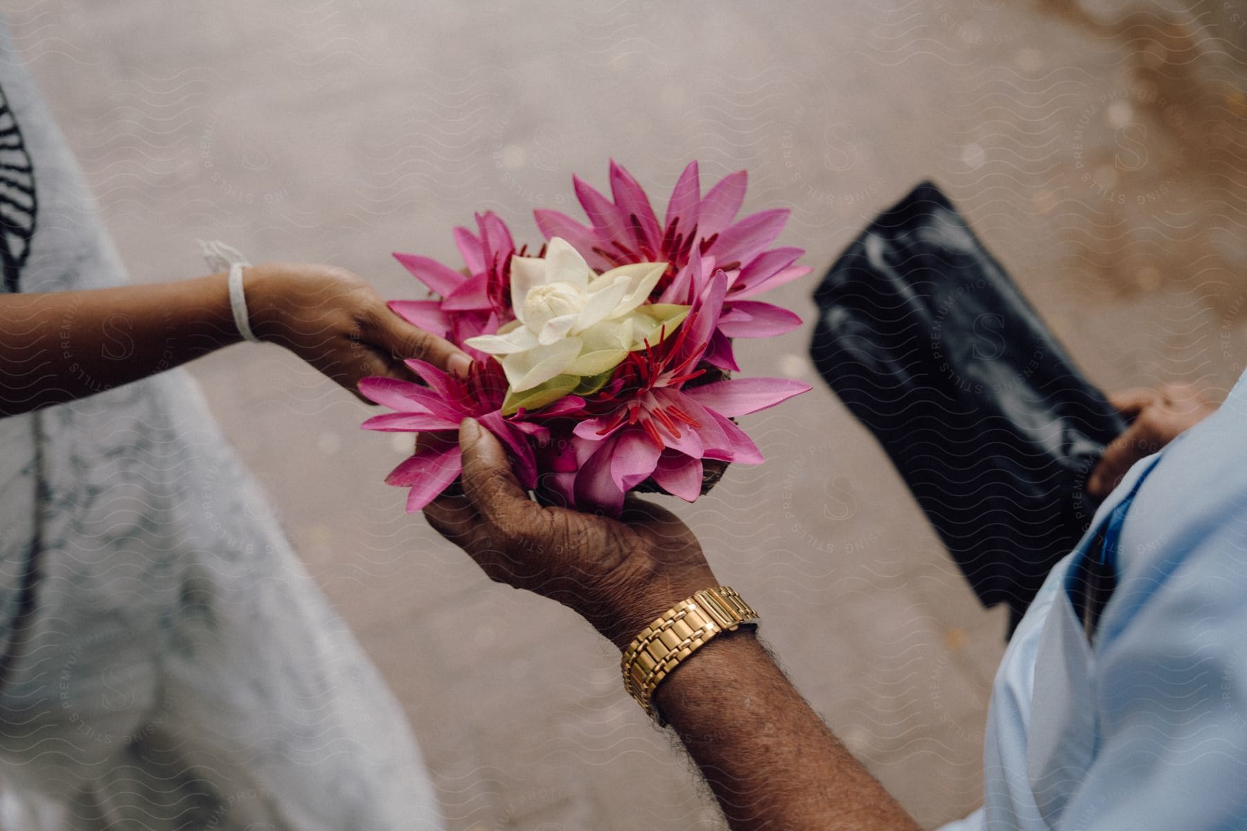 A white and pink flower bouquet held by a man and a woman, as one of them hands it to the other.