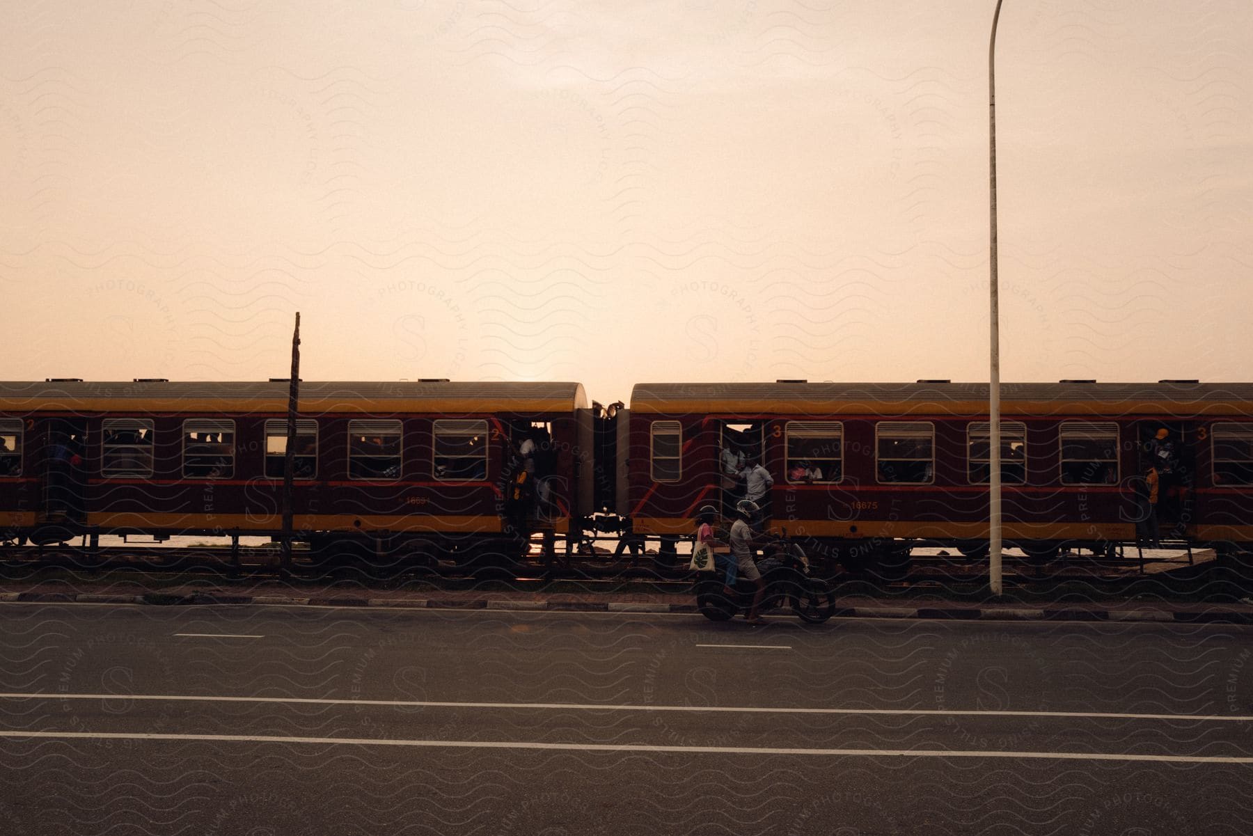 A group of people are standing on a passenger train while two people sit next to it on a motorcycle.