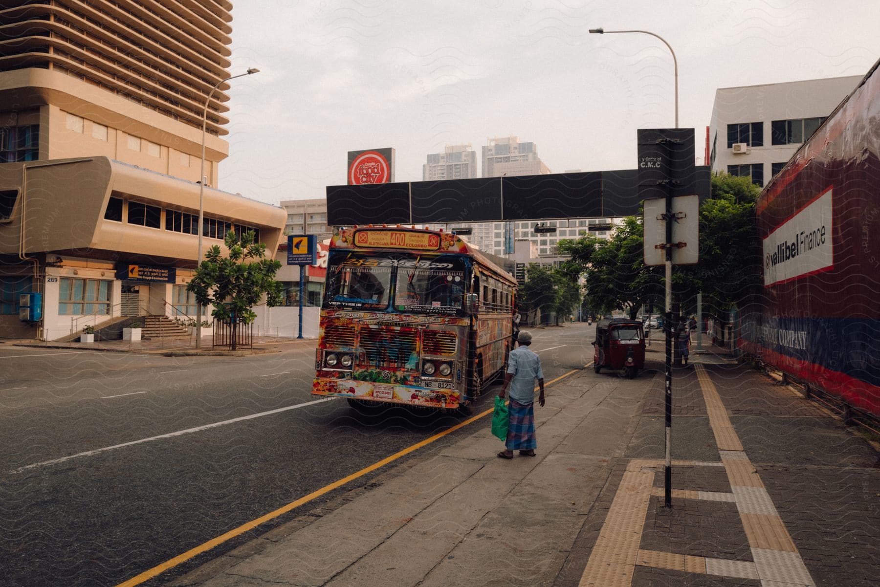 Pedestrian standing on a downtown street as a bus pulls up with tall city buildings in the distance