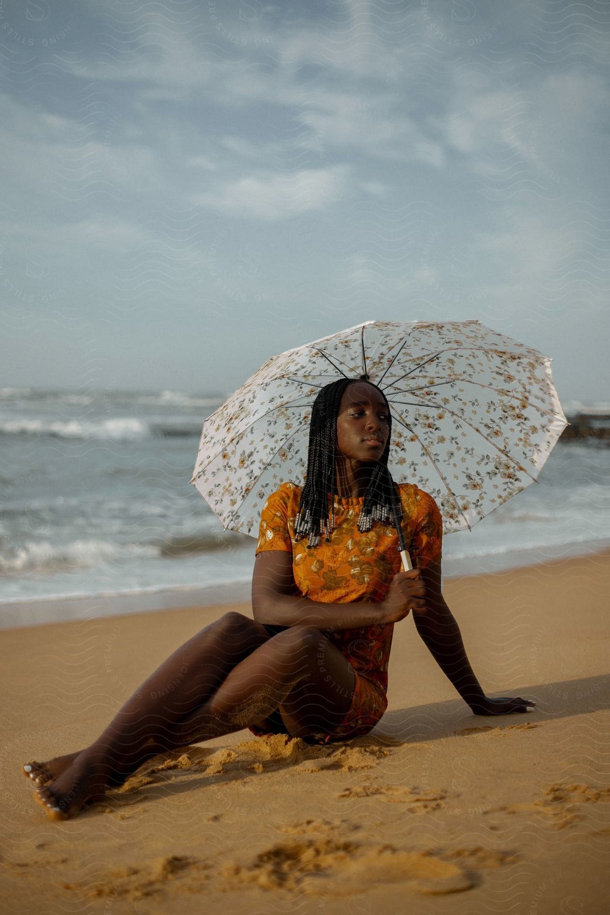 A woman is sitting on the beach sand holding a white umbrella and behind her is the sea