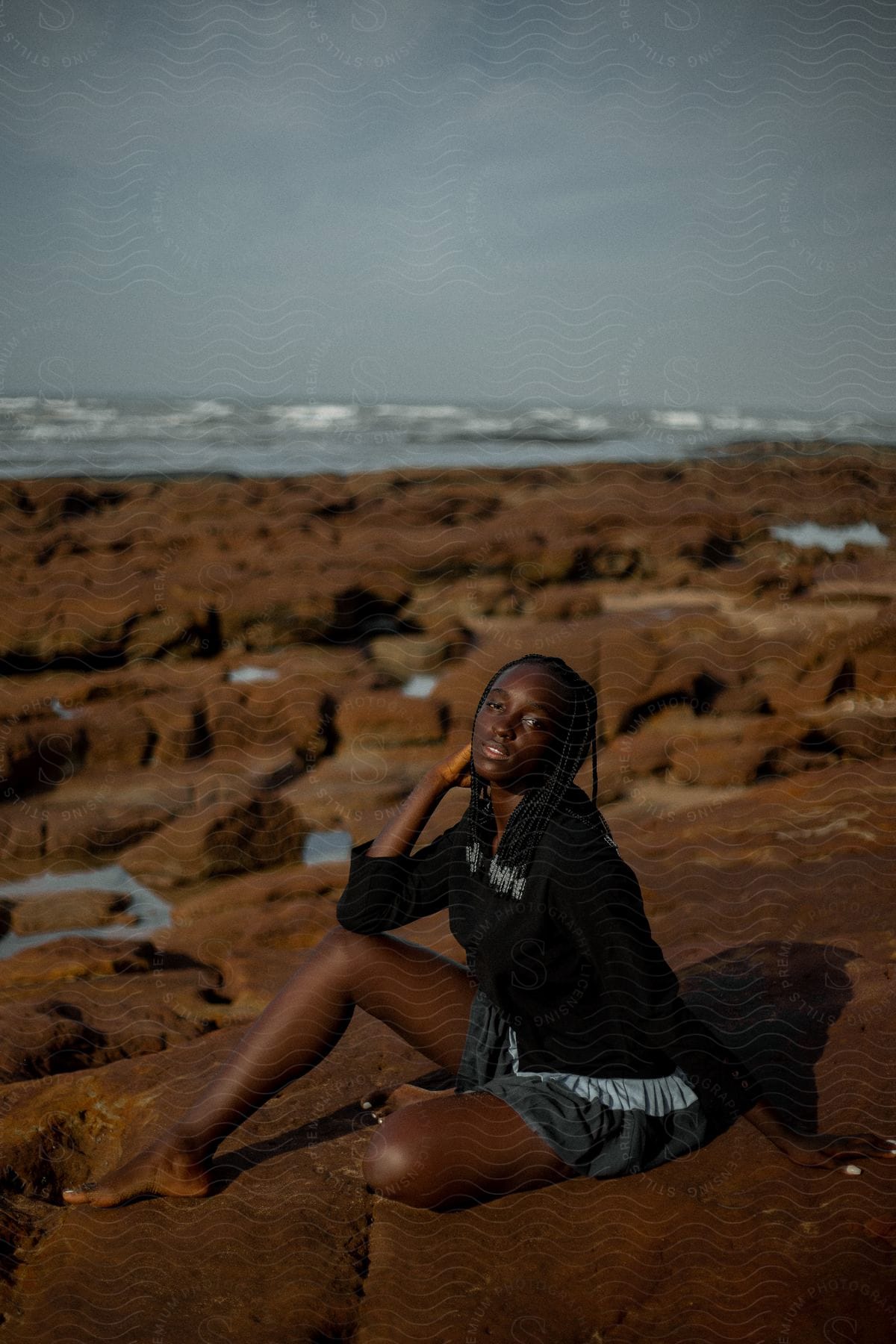 A person is sitting on rocks by the sea, posing for a photo.