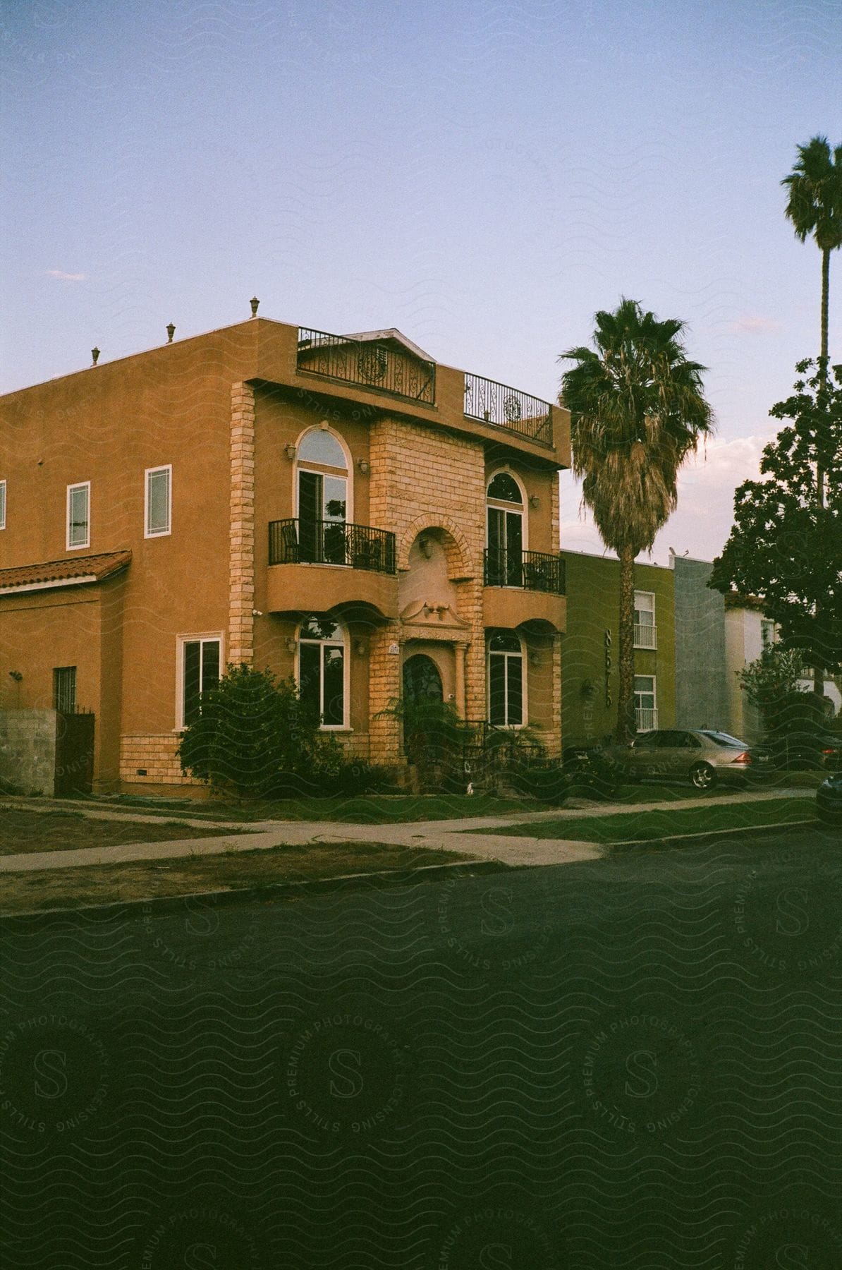 A two-story orange building with balconies is situated next to a street. A palm tree and another building are visible in the background.