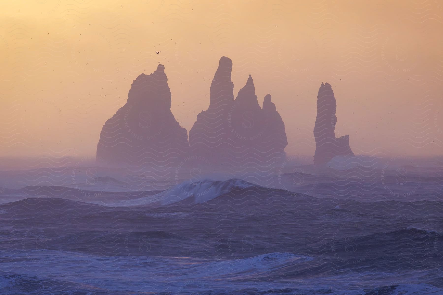 The mysterious silhouette of rock formations stands out against a softly lit sky, surrounded by a rough sea.