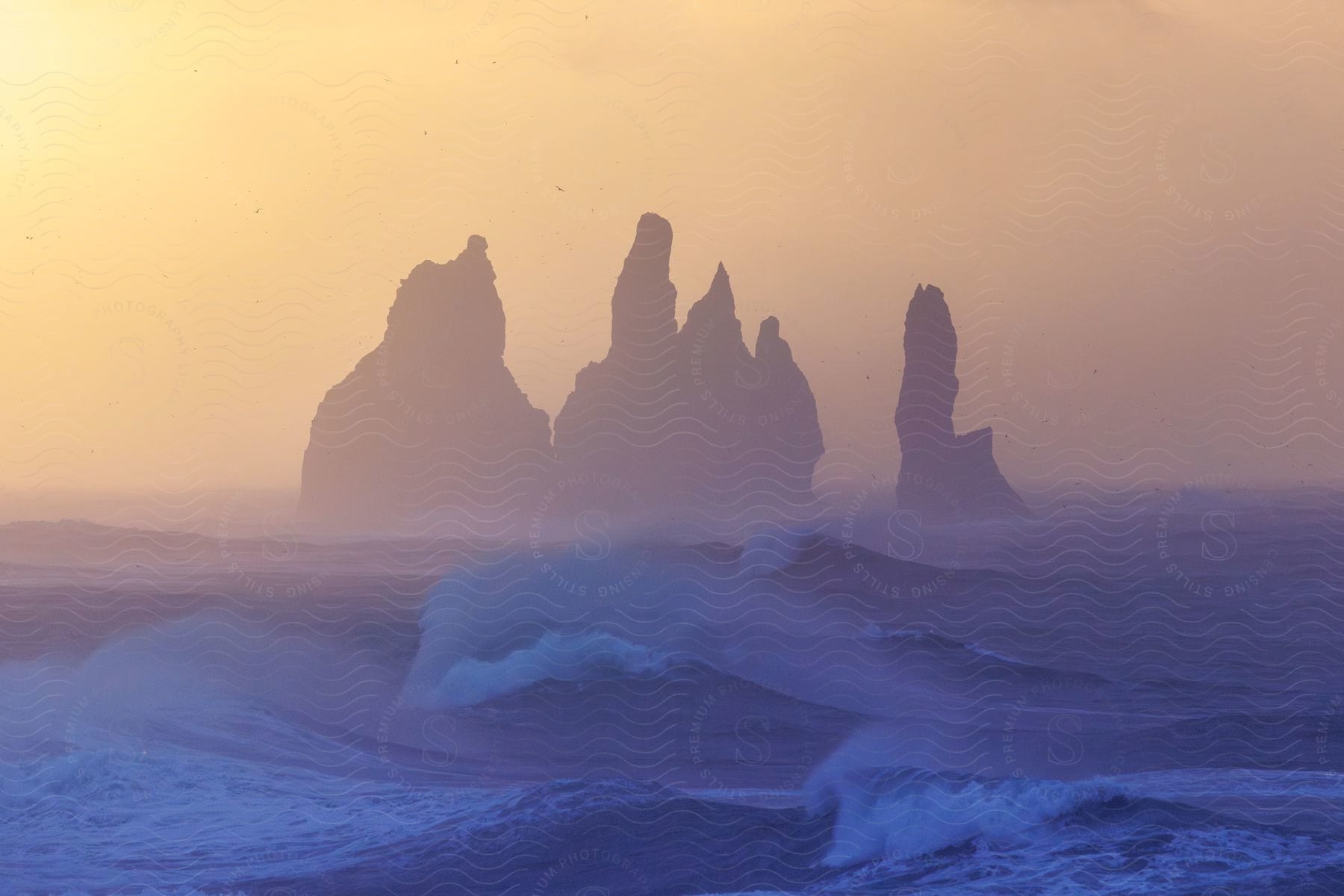 Tall rock formations along the coast as waves roll into shore on a foggy day