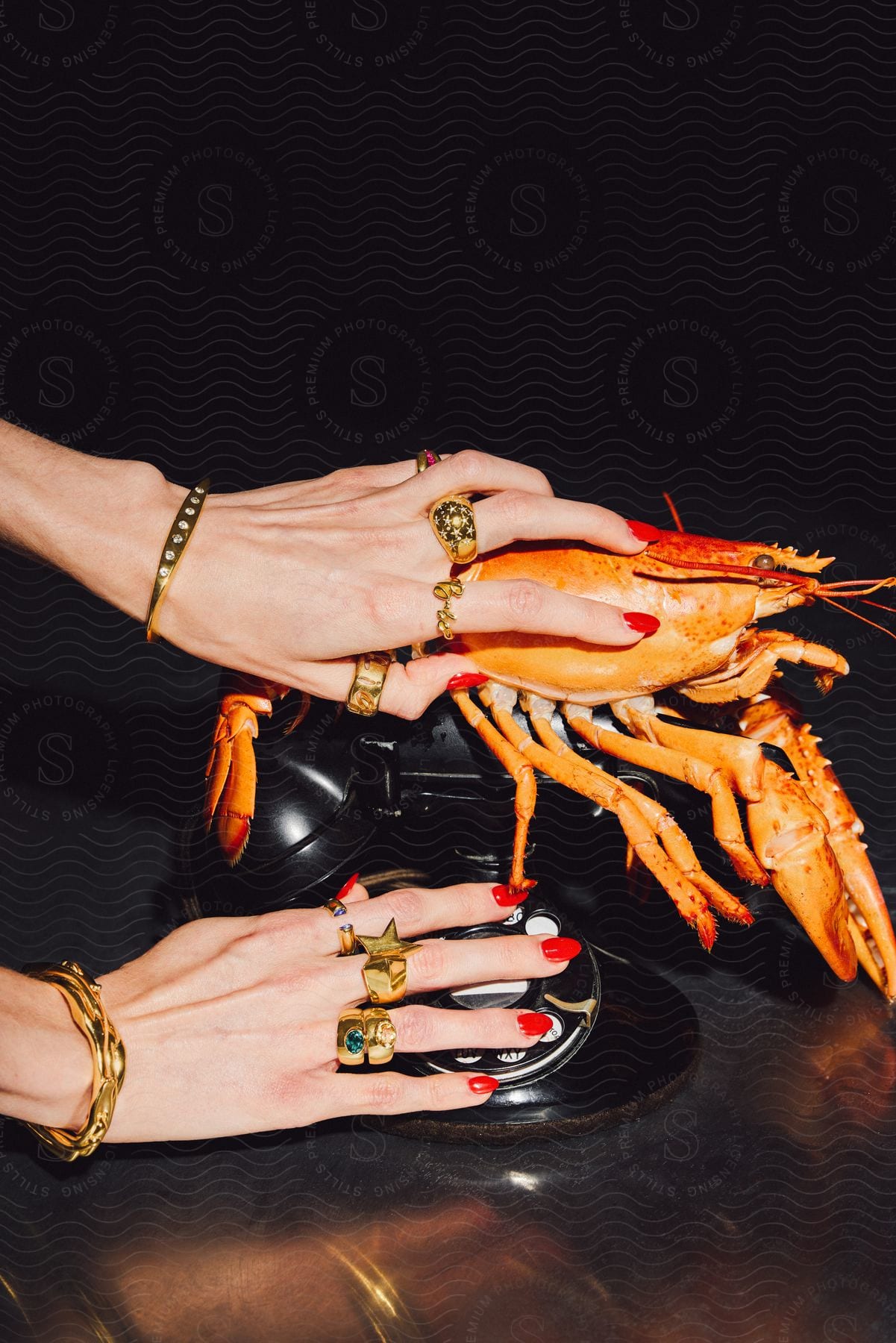 The ringed hands of a woman placing a cooked lobster on top of an old rotary phone.