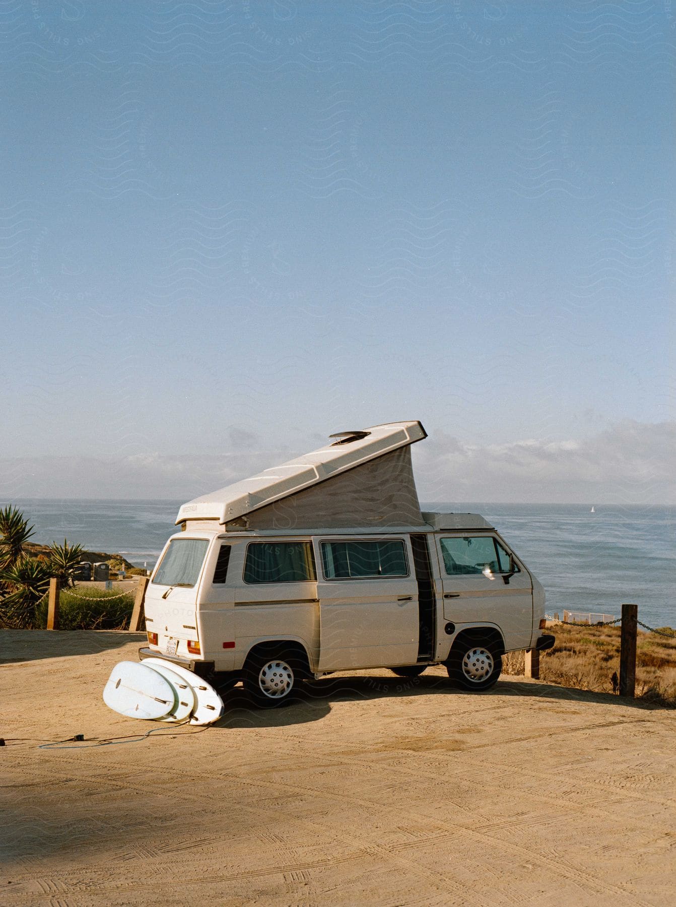 A white conversion van parked on the coast with surfboards laid out in the back.