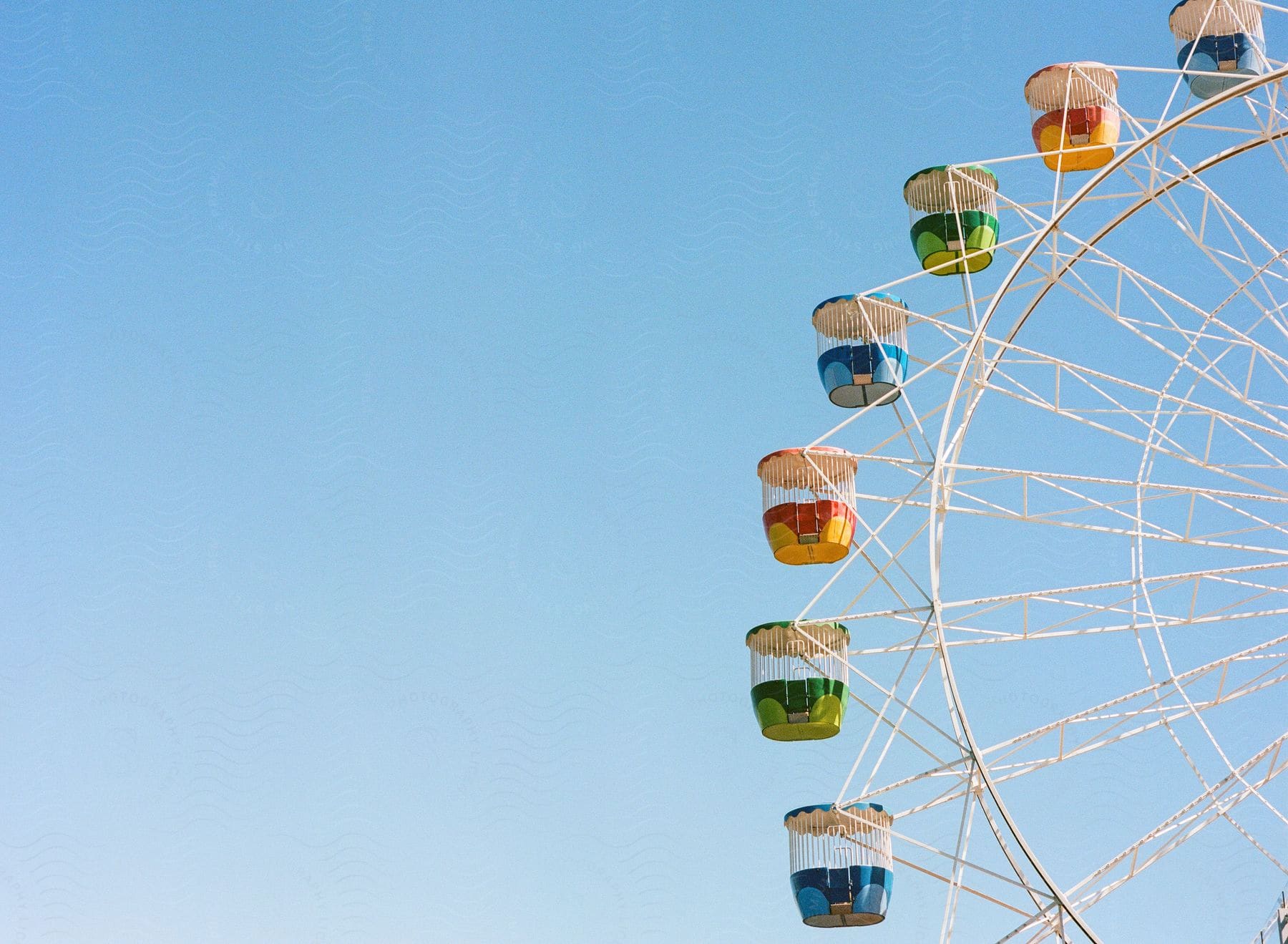 A colorful Ferris wheel, with different colored cabins, stands out against a clear blue sky.