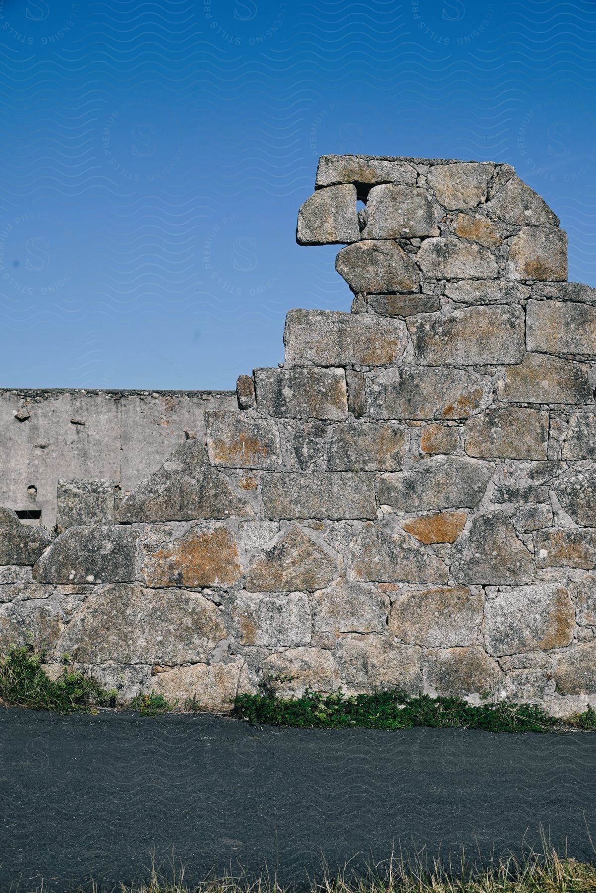Exterior architecture of a rock wall next to an asphalt against a cloudless blue sky