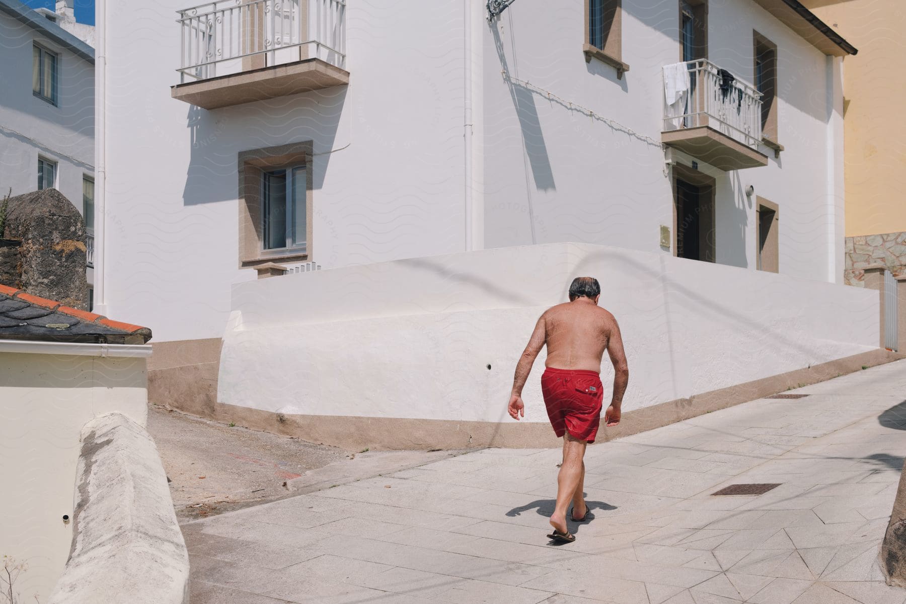 Man without a t-shirt and in red shorts walking through a residential neighborhood