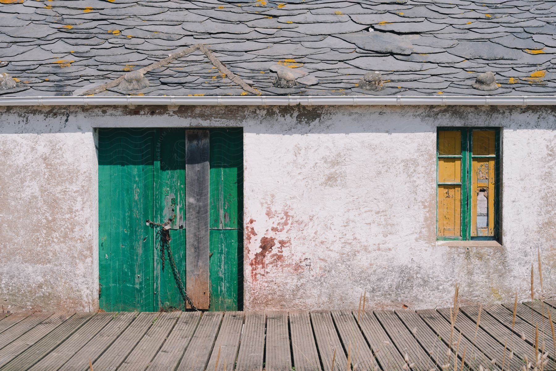 A weathered house with a bright yellow window and a chained green door.