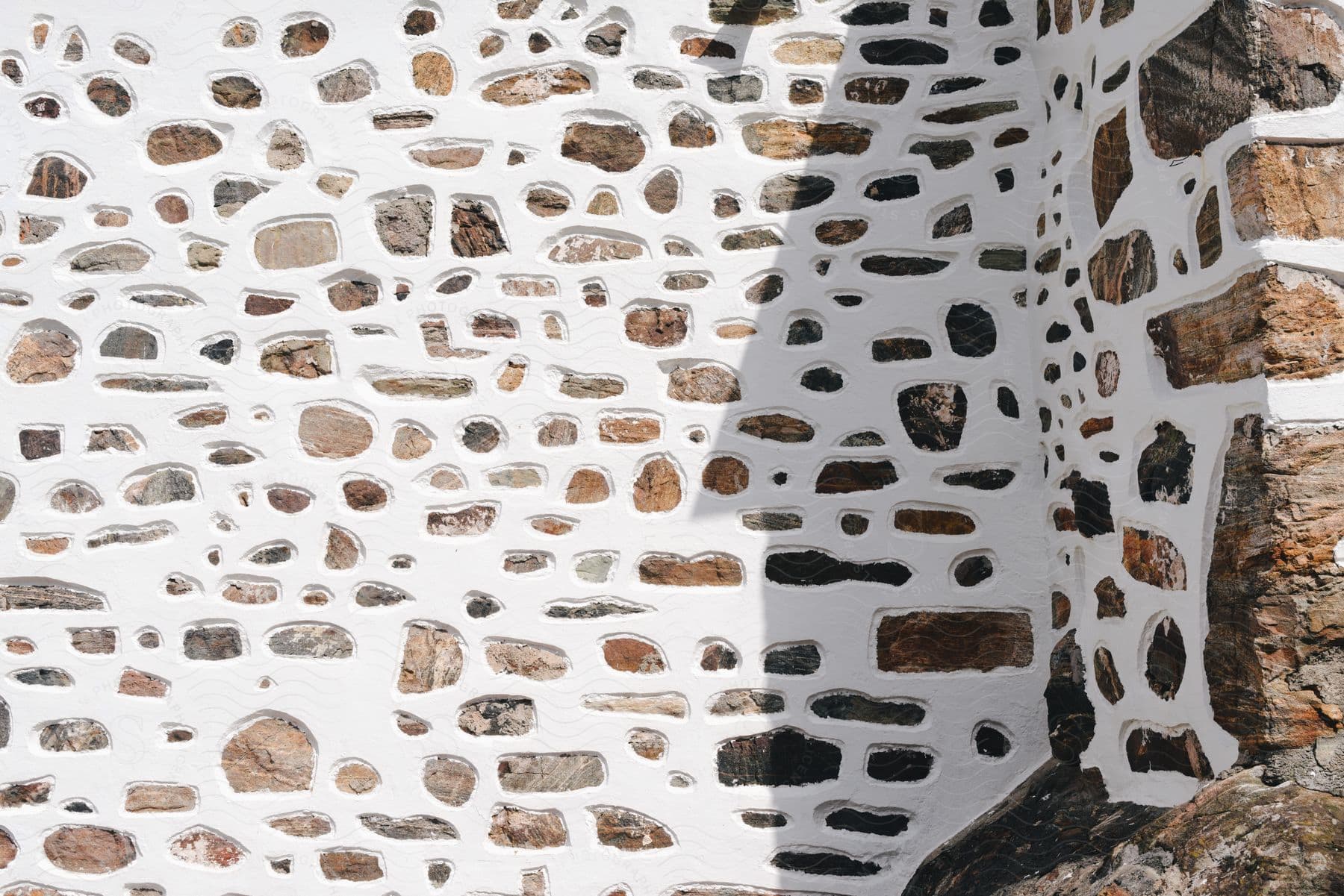 White stucco forms pattern on surface of  exterior stone wall near a corner.