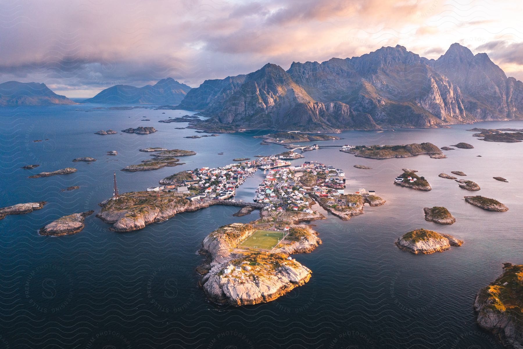 A small island village of Henningsvaer nestles amidst mountains and water, with a few boats bobbing below a cloudy sky