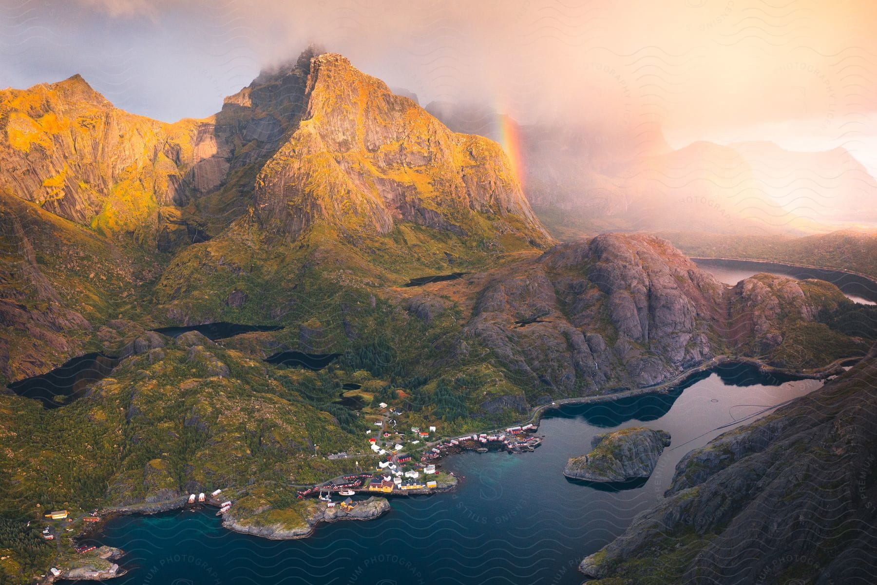 Natural landscape with mountains and a small village located along the coast by a lake on a day with a red sky and rainbows.