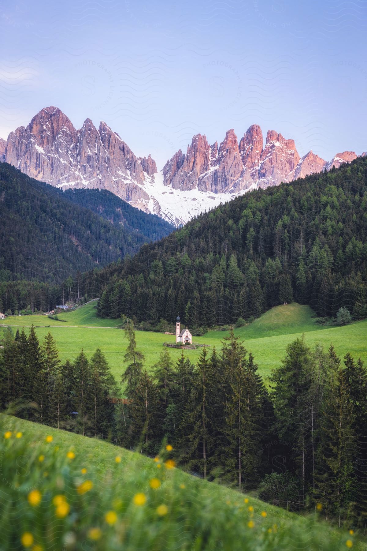 The Church of Saint John in Italy sitting at the base of green hills with mountains behind