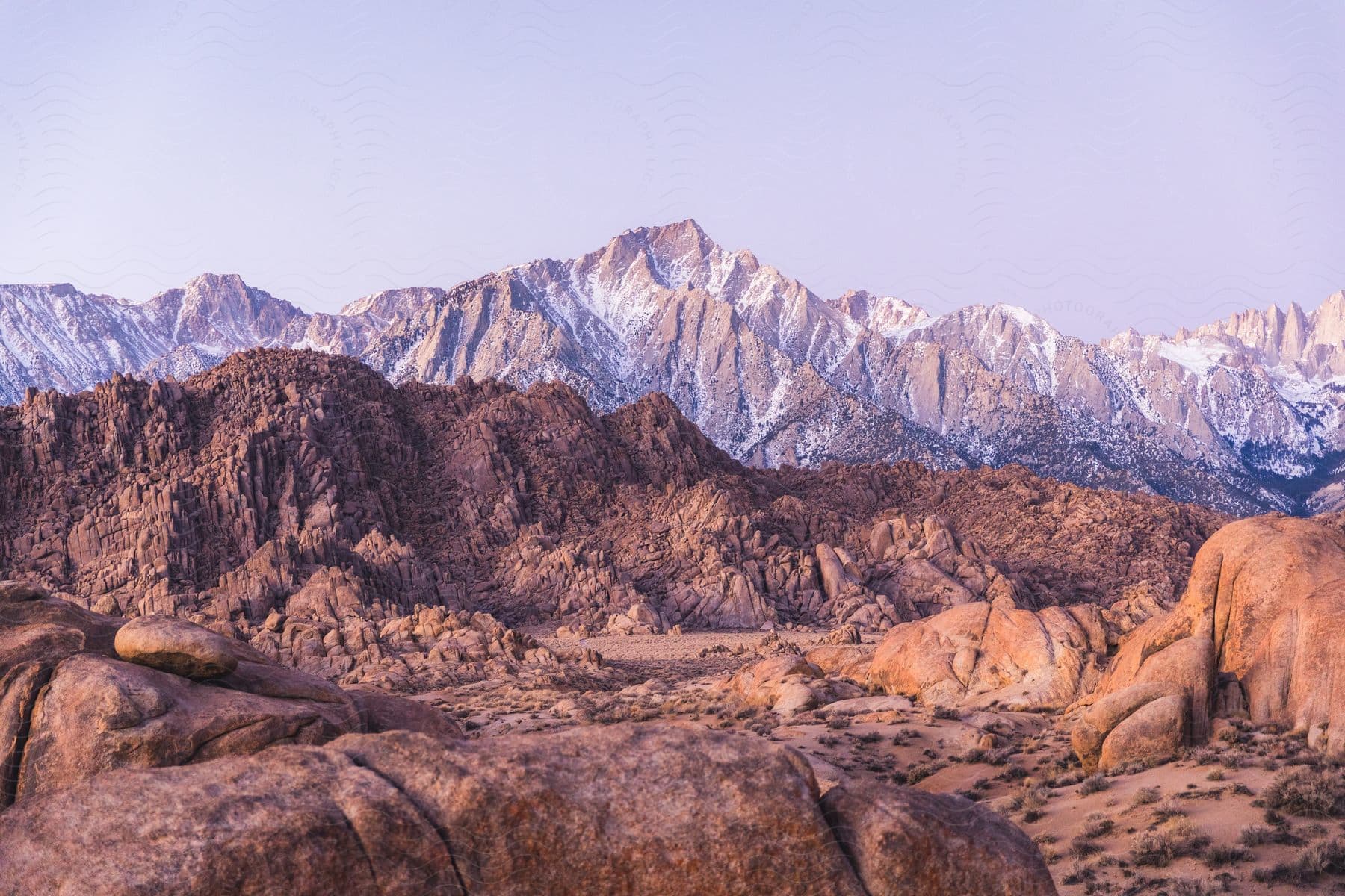 A vast landscape of weathered, rounded boulders stretches towards a backdrop of snow-capped mountains.