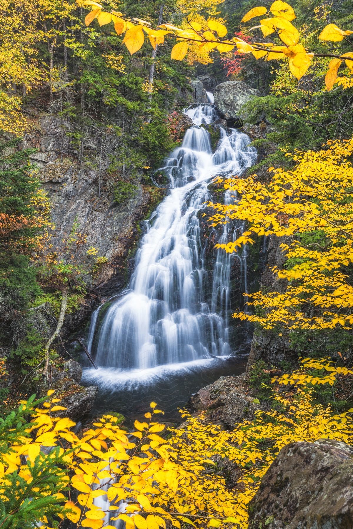 Crystal Cascade plunges down a rocky cliff surrounded by colorful autumn foliage.