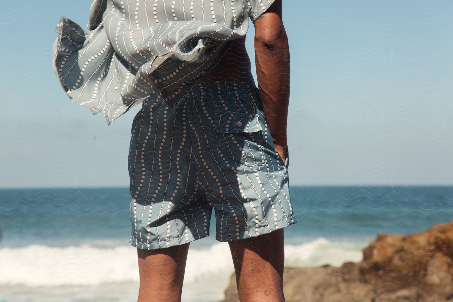 Man standing on the beach wearing shorts against a clear blue sky.