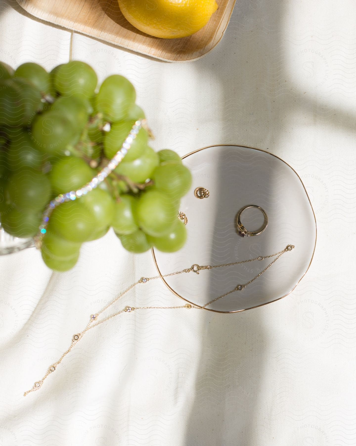 Green grapes are dangling over a ceramic plate with jewelry.