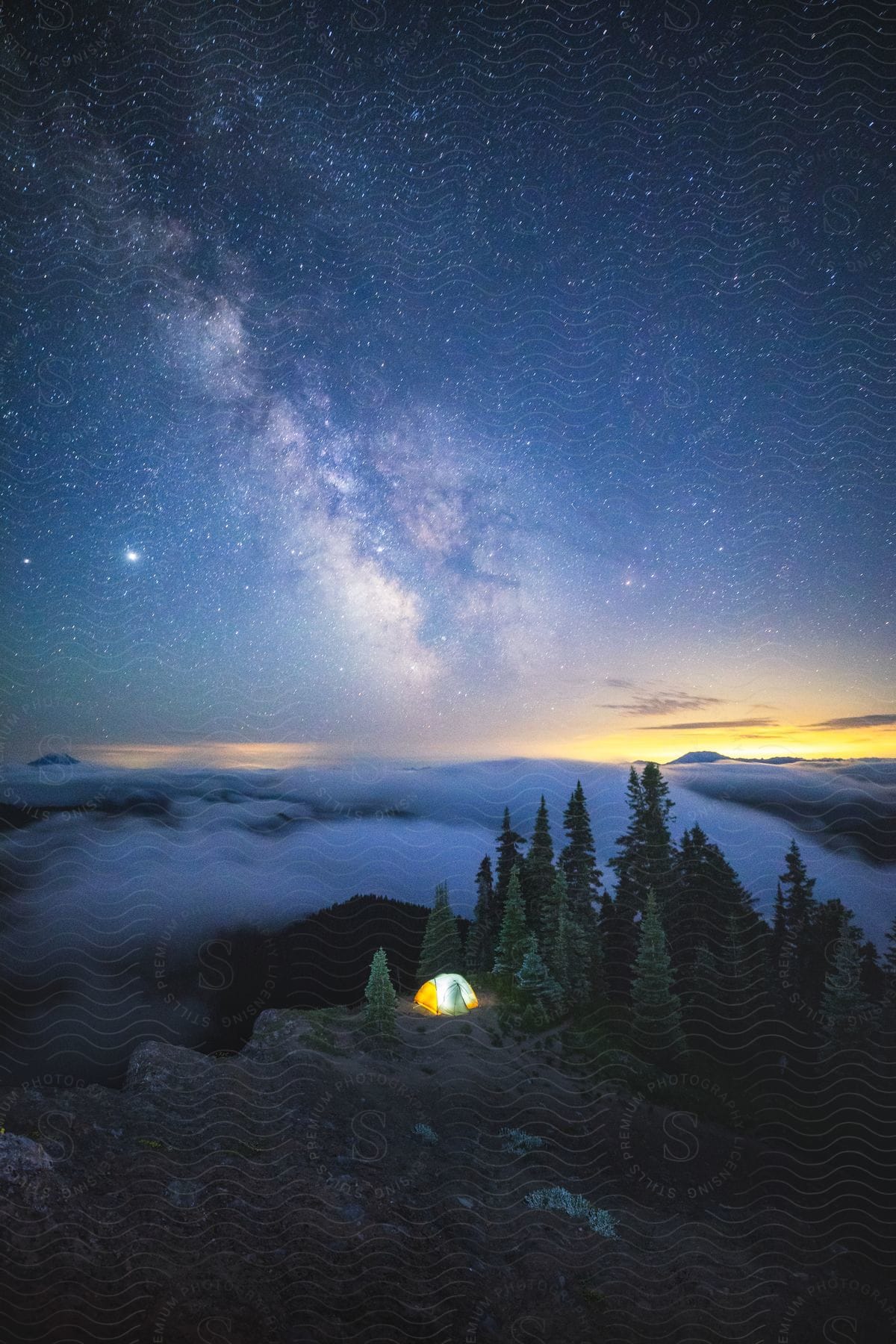 A tent illuminated under a starry sky and a sunrise on the horizon
