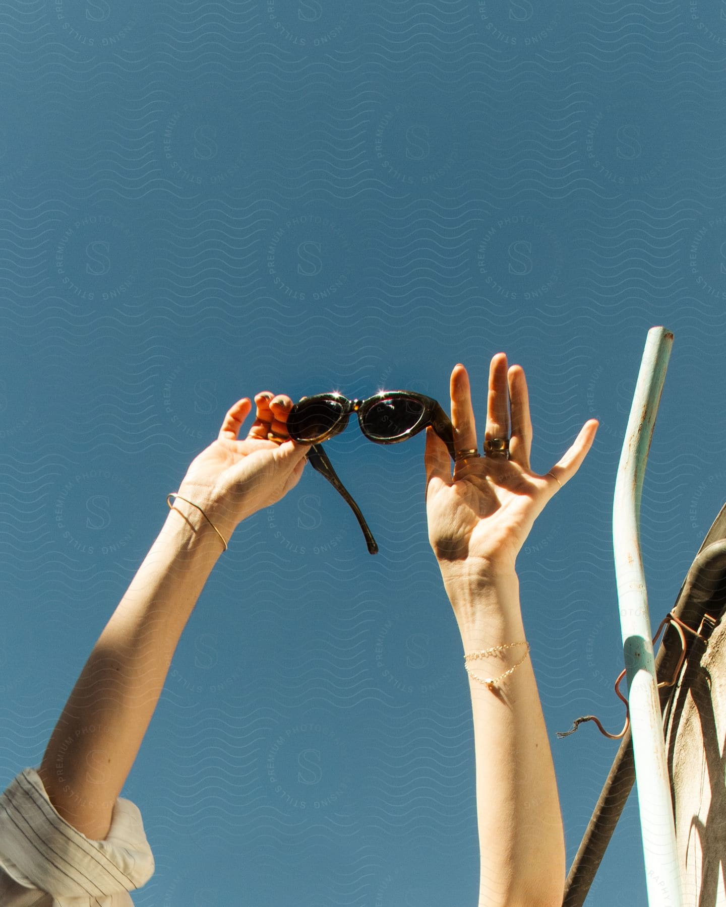 Two hands hold a pair of sunglasses against blue sky background